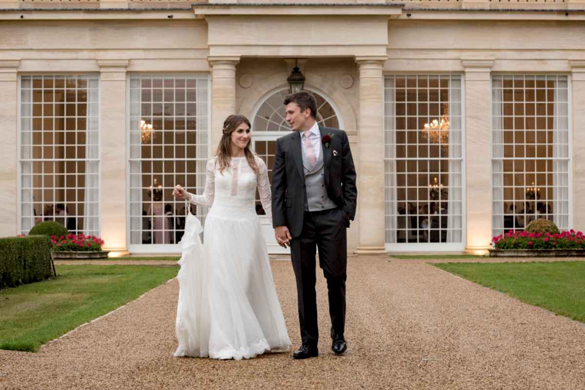 Bride & groom walking in front of the Orangery at Rushton Hall in Northants