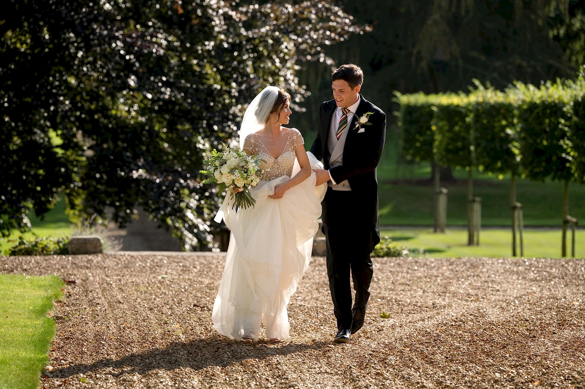 Groom carrying bride's train as she walks