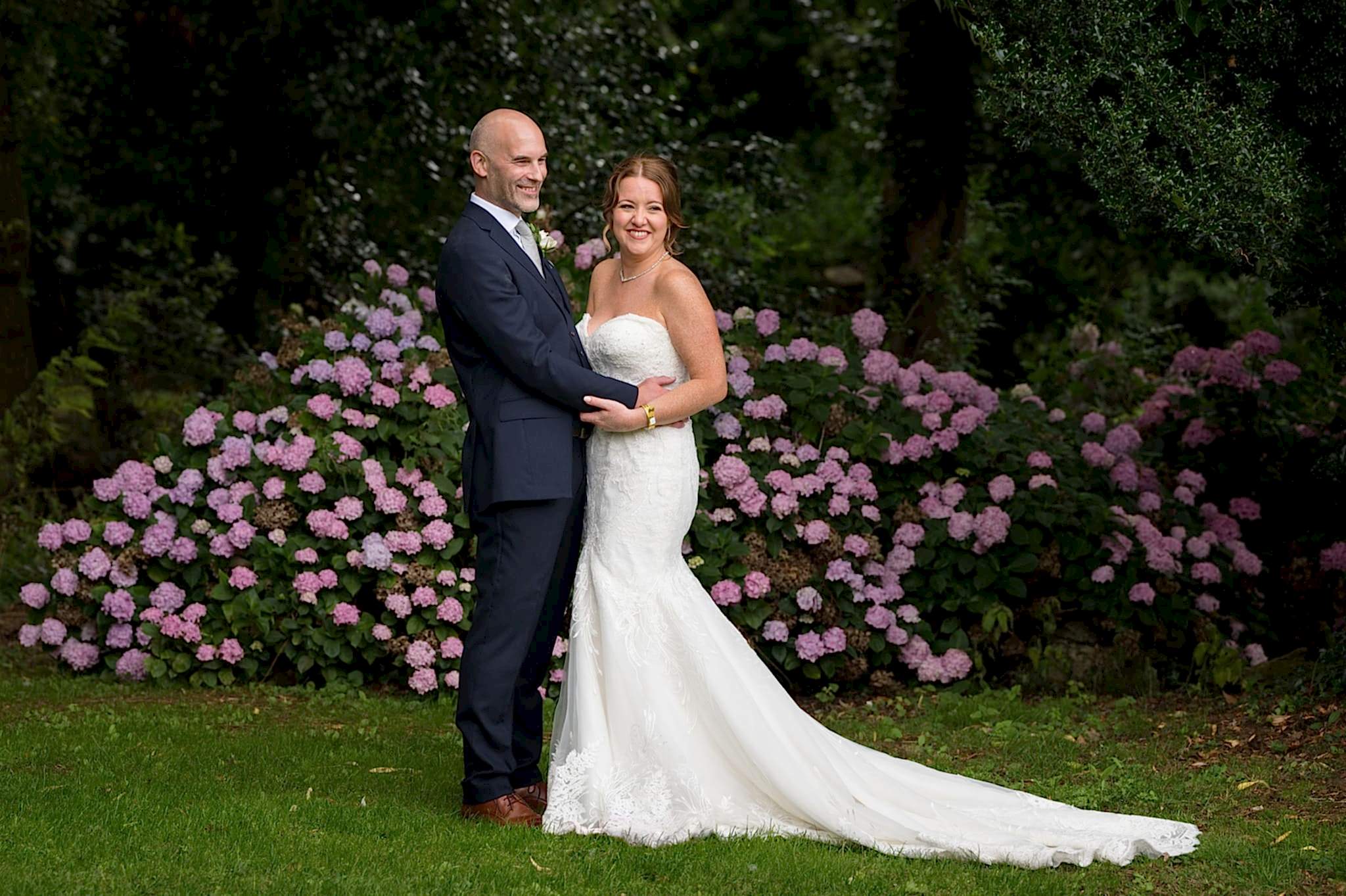 Couple standing in front of pink hydrangea bush