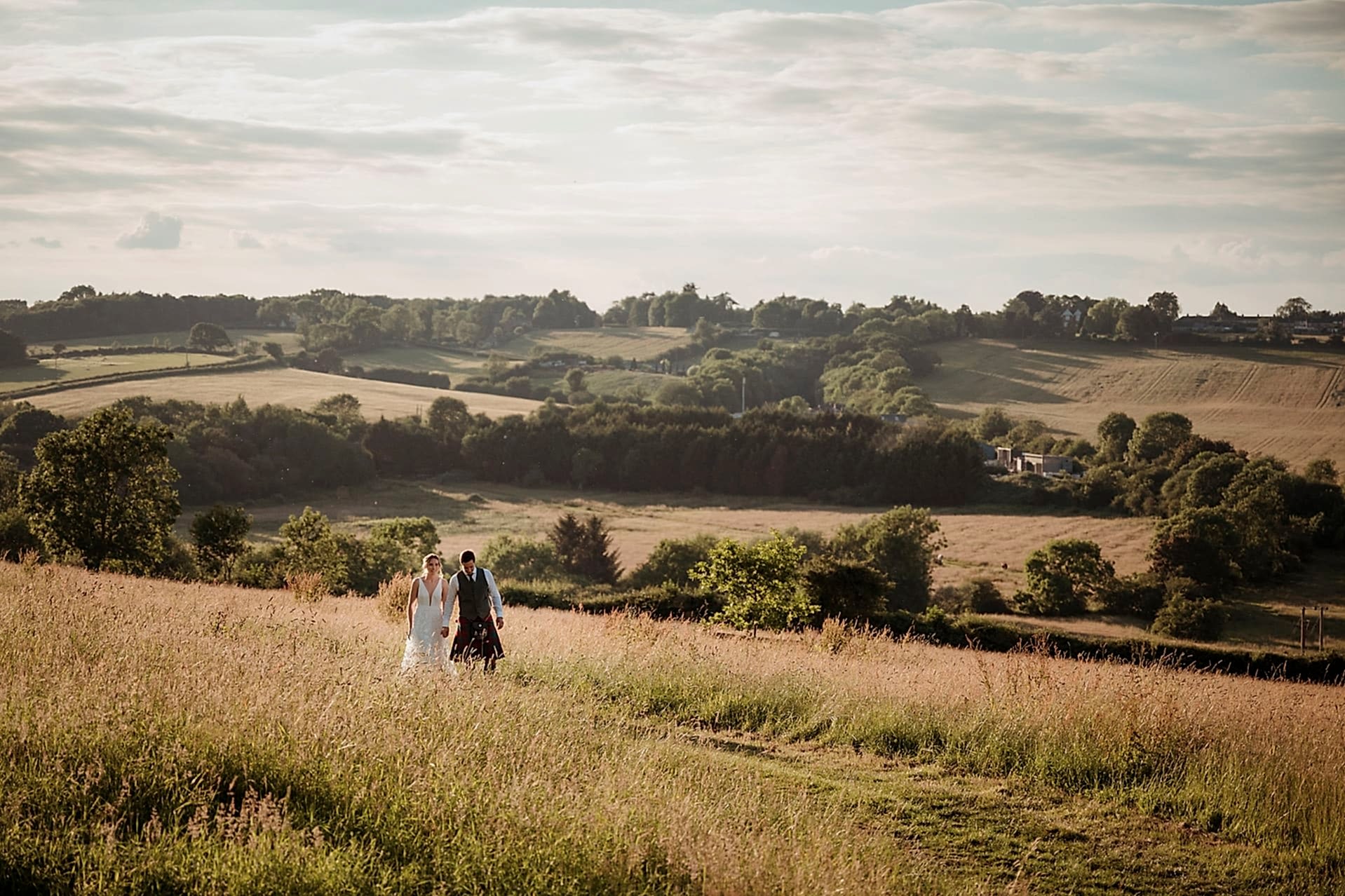 Bride and groom walking through a field during golden hour