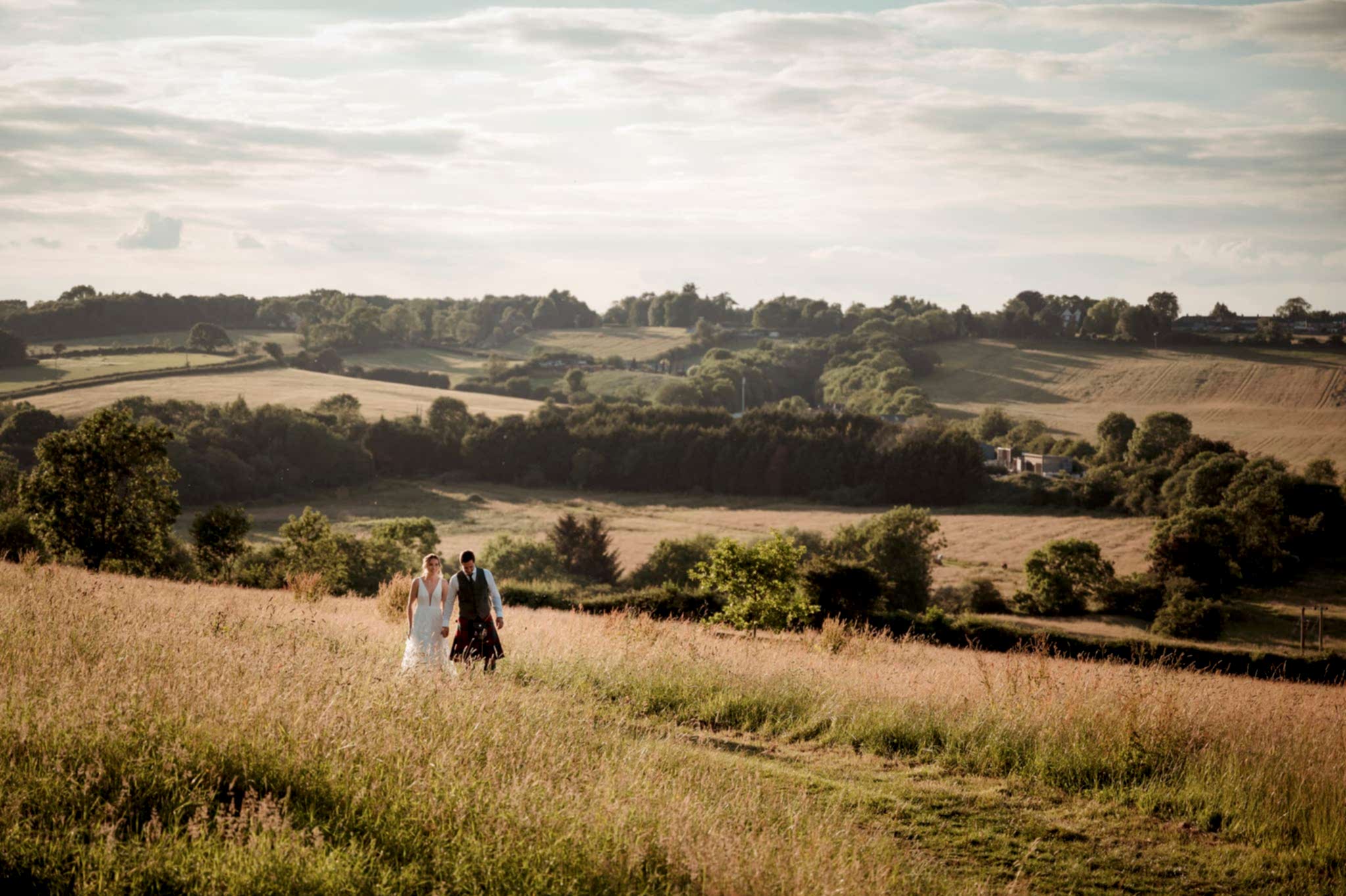 Bride and groom walking through a field during golden hour