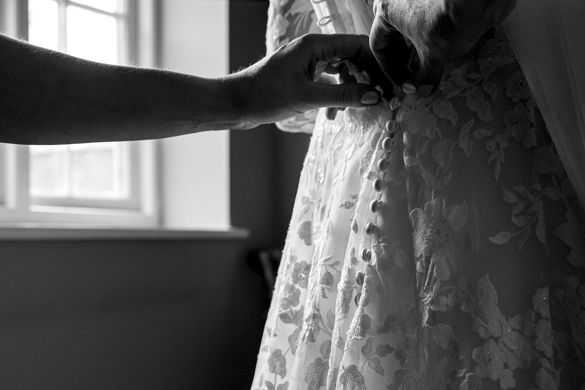 Close up shot of someone's fingers doing up little buttons on the back of a bride's dress