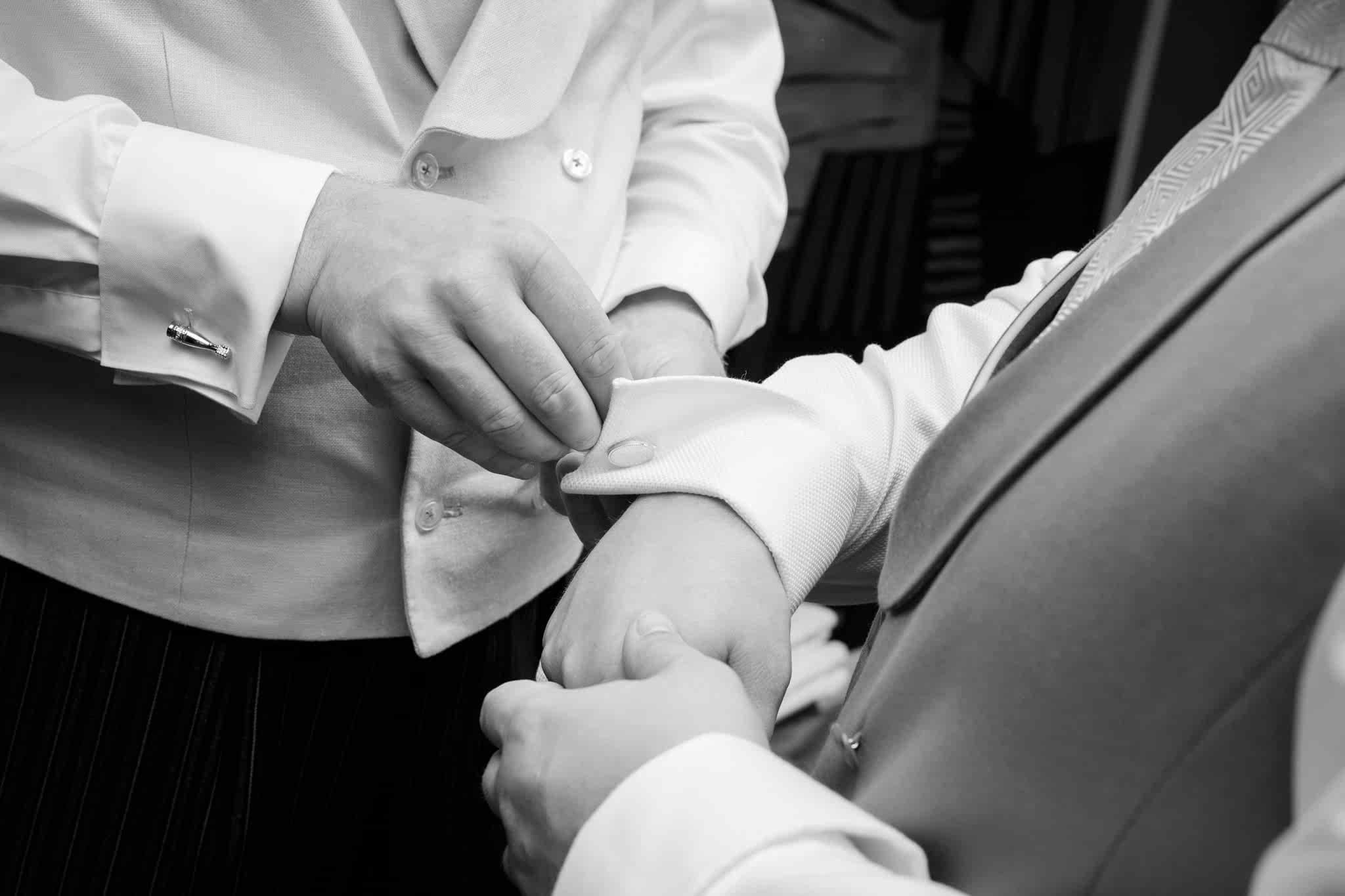 A close up shot of the best man's hands putting the groom's cufflinks on