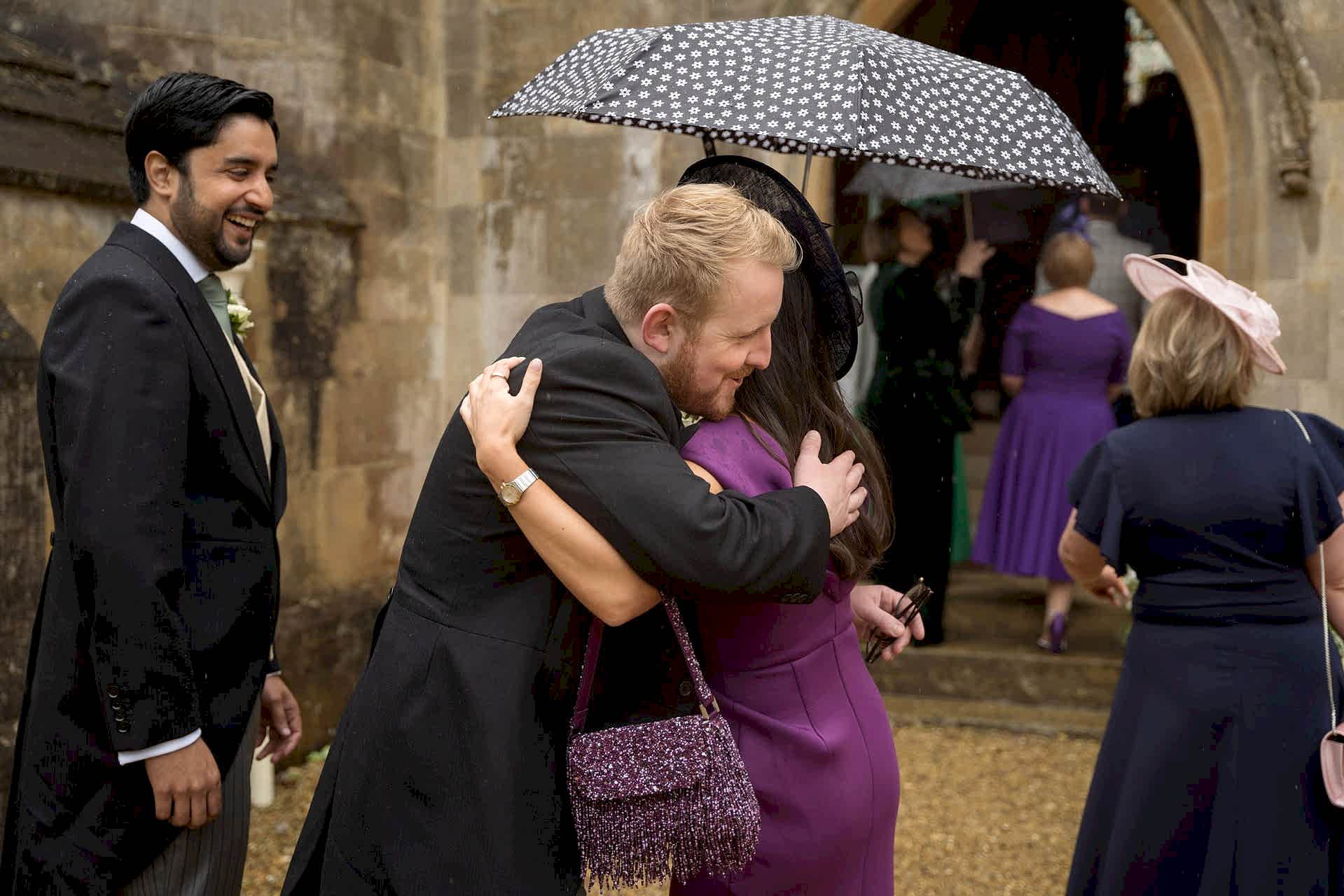 Wedding guests greeting each other with a hug as they arrive at Exton Park chapel