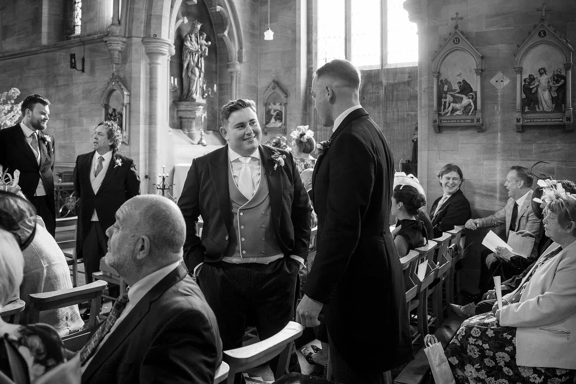 The groom chatting with a wedding guest inside Exton Park chapel before the ceremony