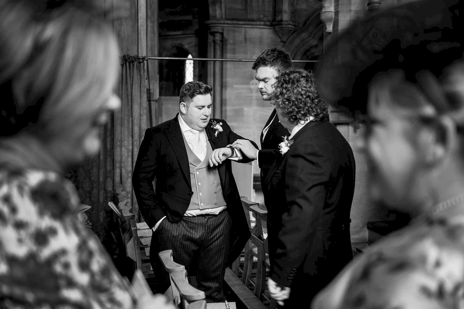 The groom checking the time on his watch as wedding guests take their seats for the ceremony