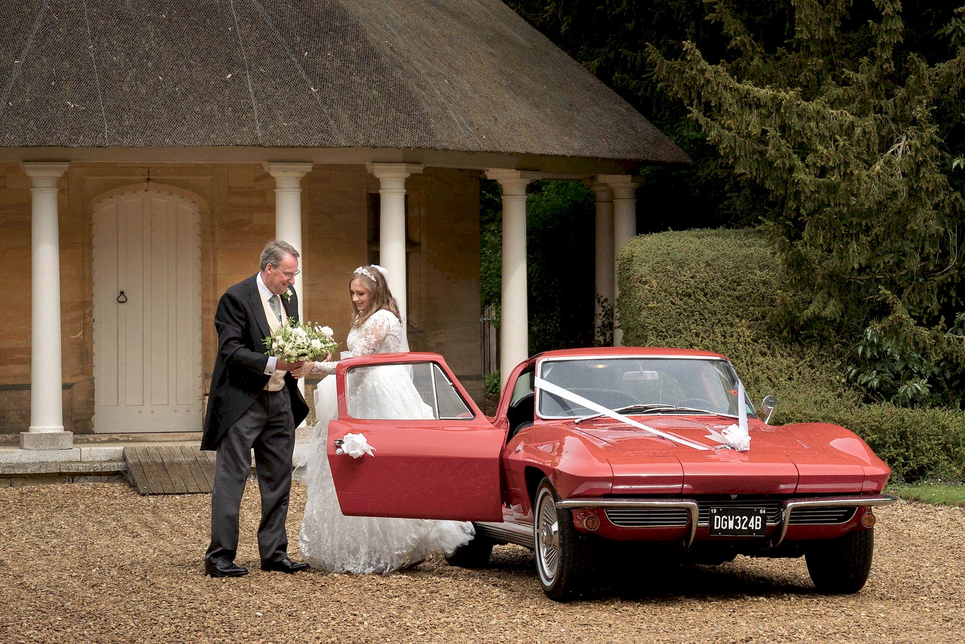 The bride arriving in a red vintage sports car at Exton Park chapel