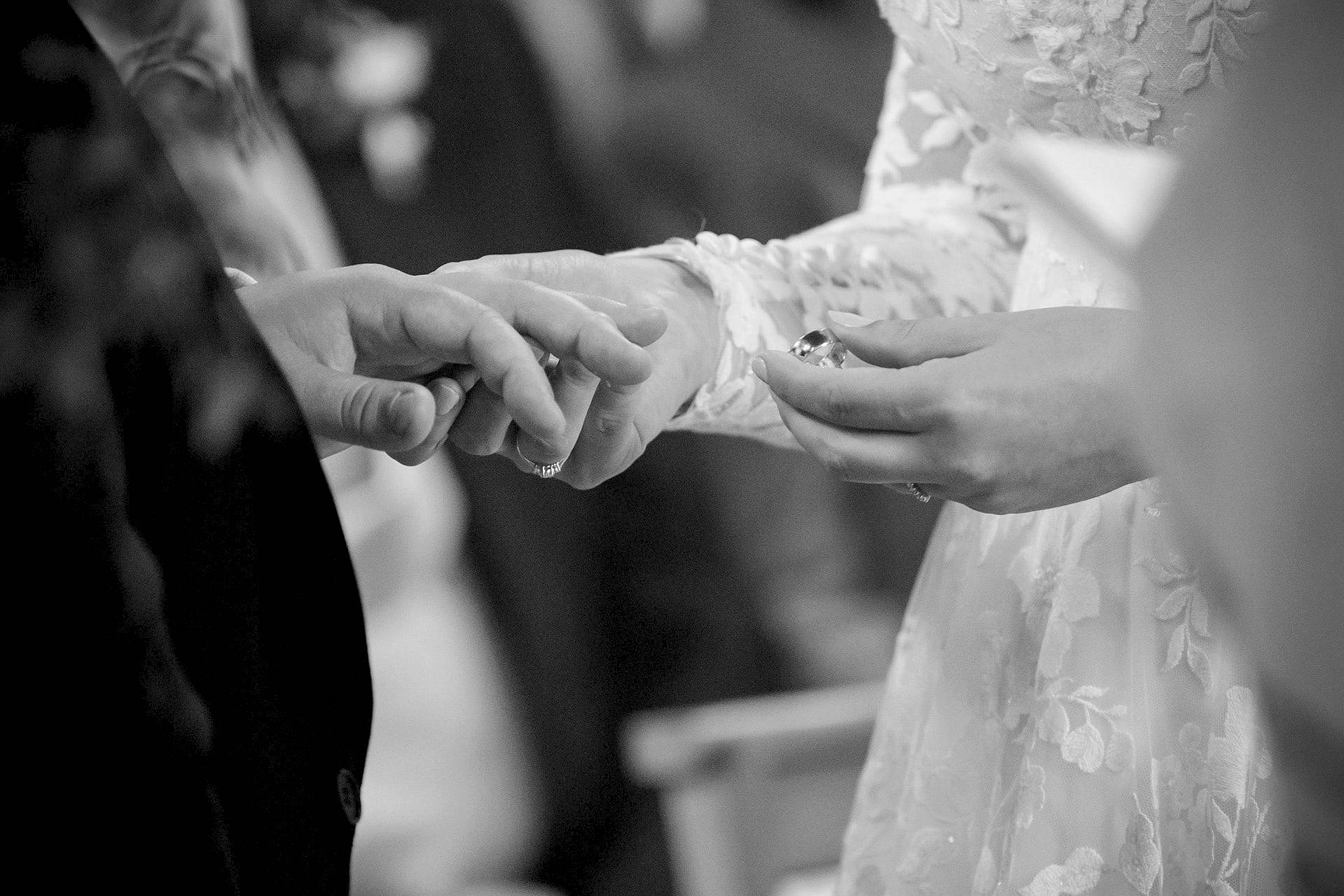 A close up shot of the groom's ring in the bride's hand just before she puts it on his fimger