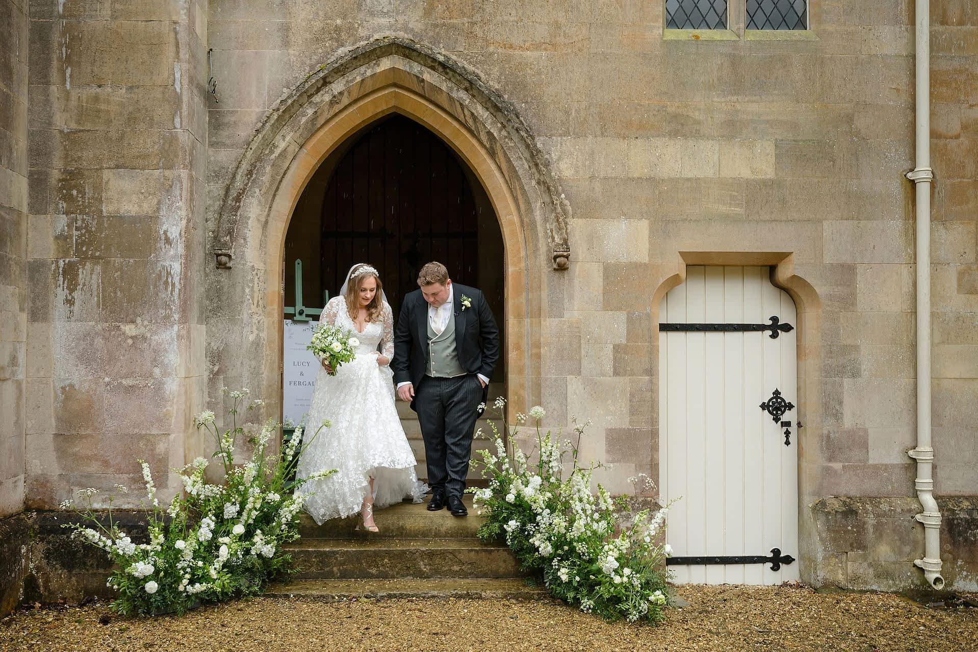 Bride and groom walking down the steps as they come out of Exton Park chapel