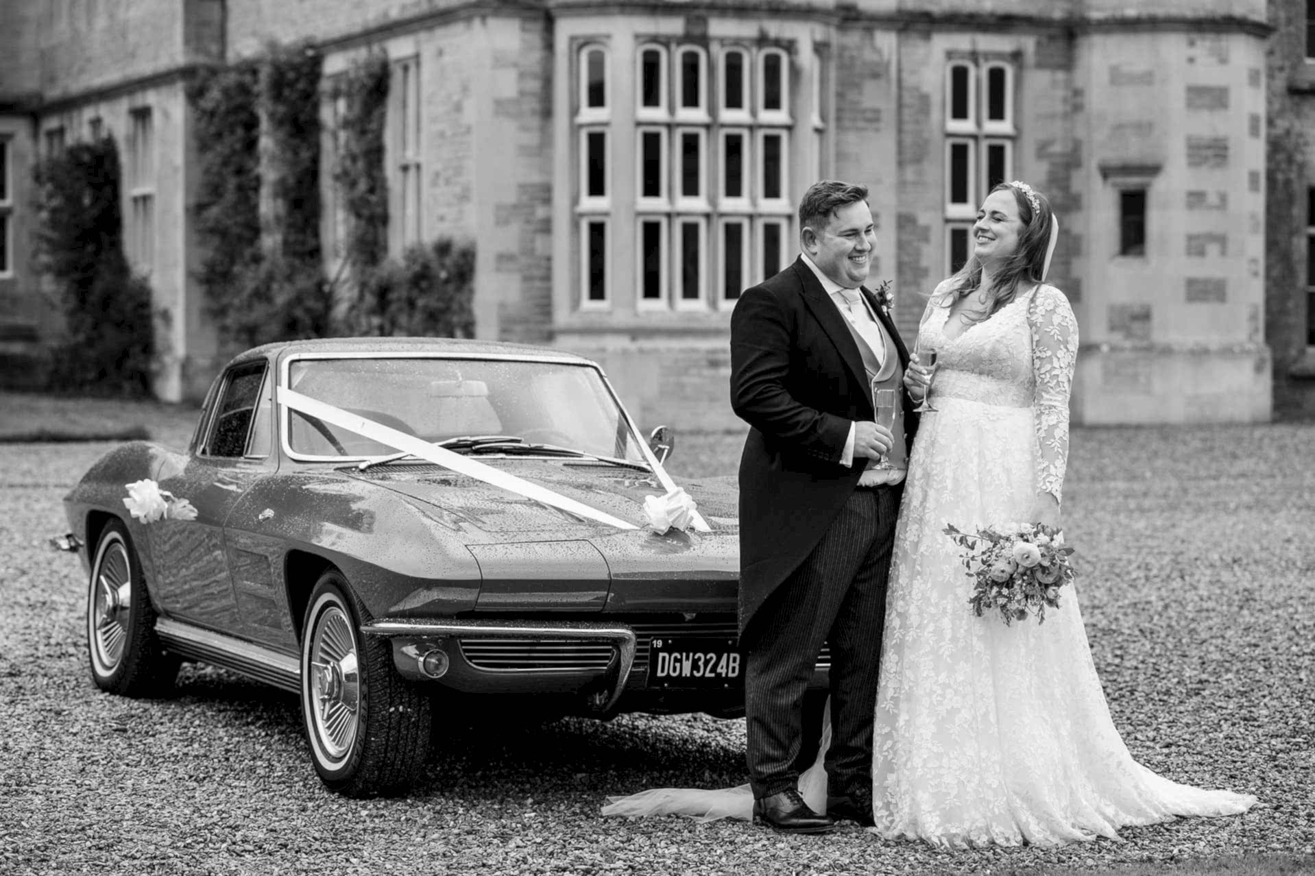 Bride and groom standing by their red vintage wedding car outside Exton Park Hall