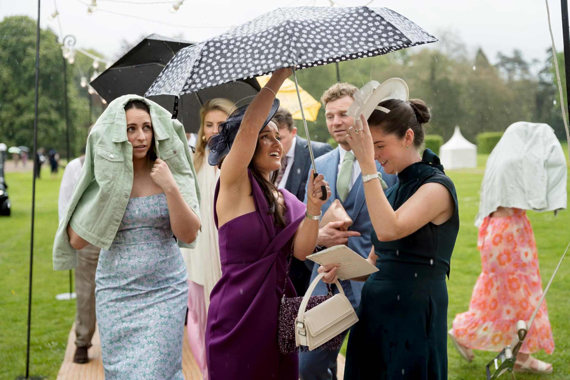 Wedding guests walking to the marquee under umbrellas in the rain at Exton Park