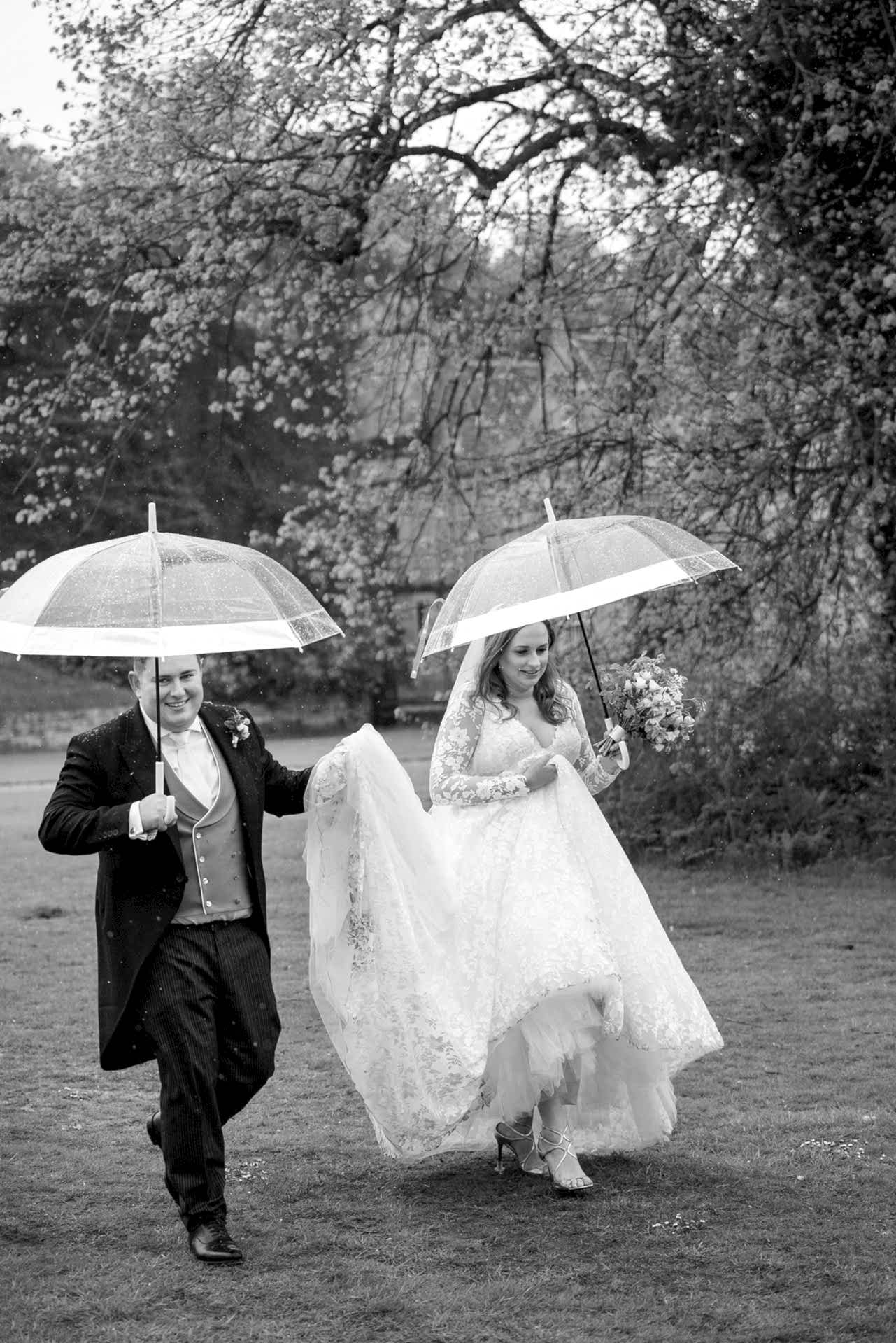 Bride and groom walking under umbrellas in the rain at Exton Park