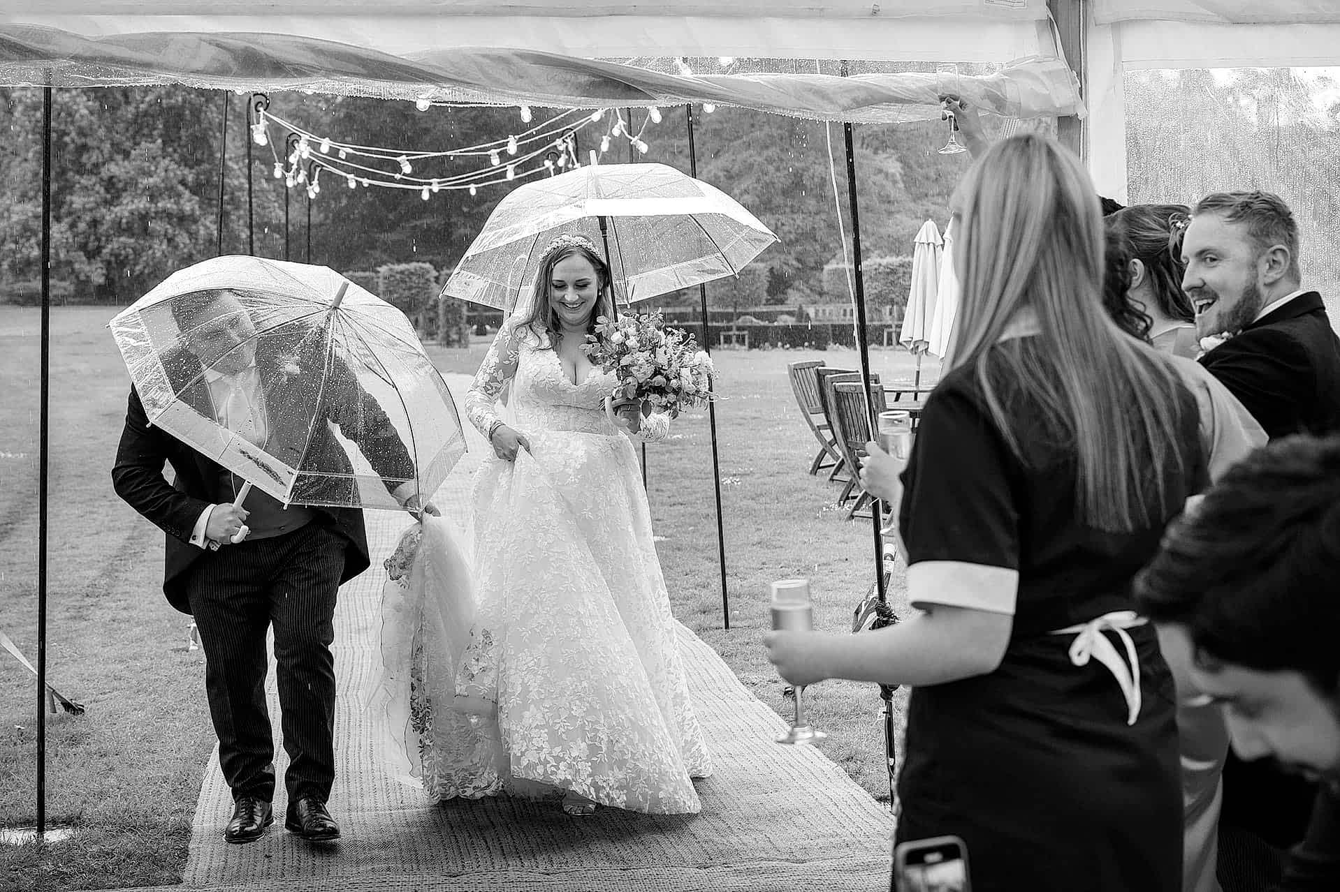 Bride and groom walking into their marquee under umbrellas