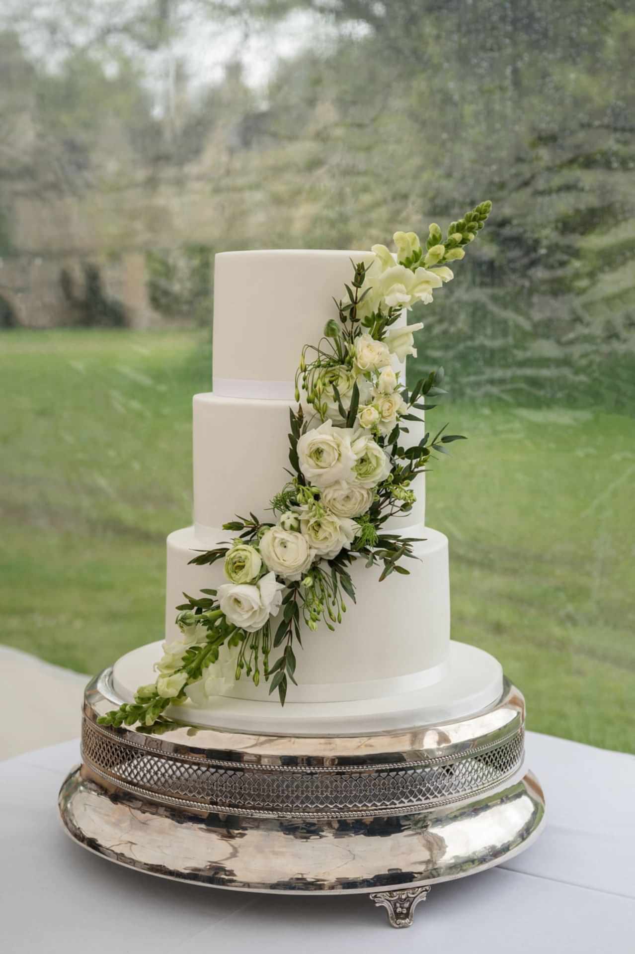 A white iced wedding cake with a spray of white flowers and foliage
