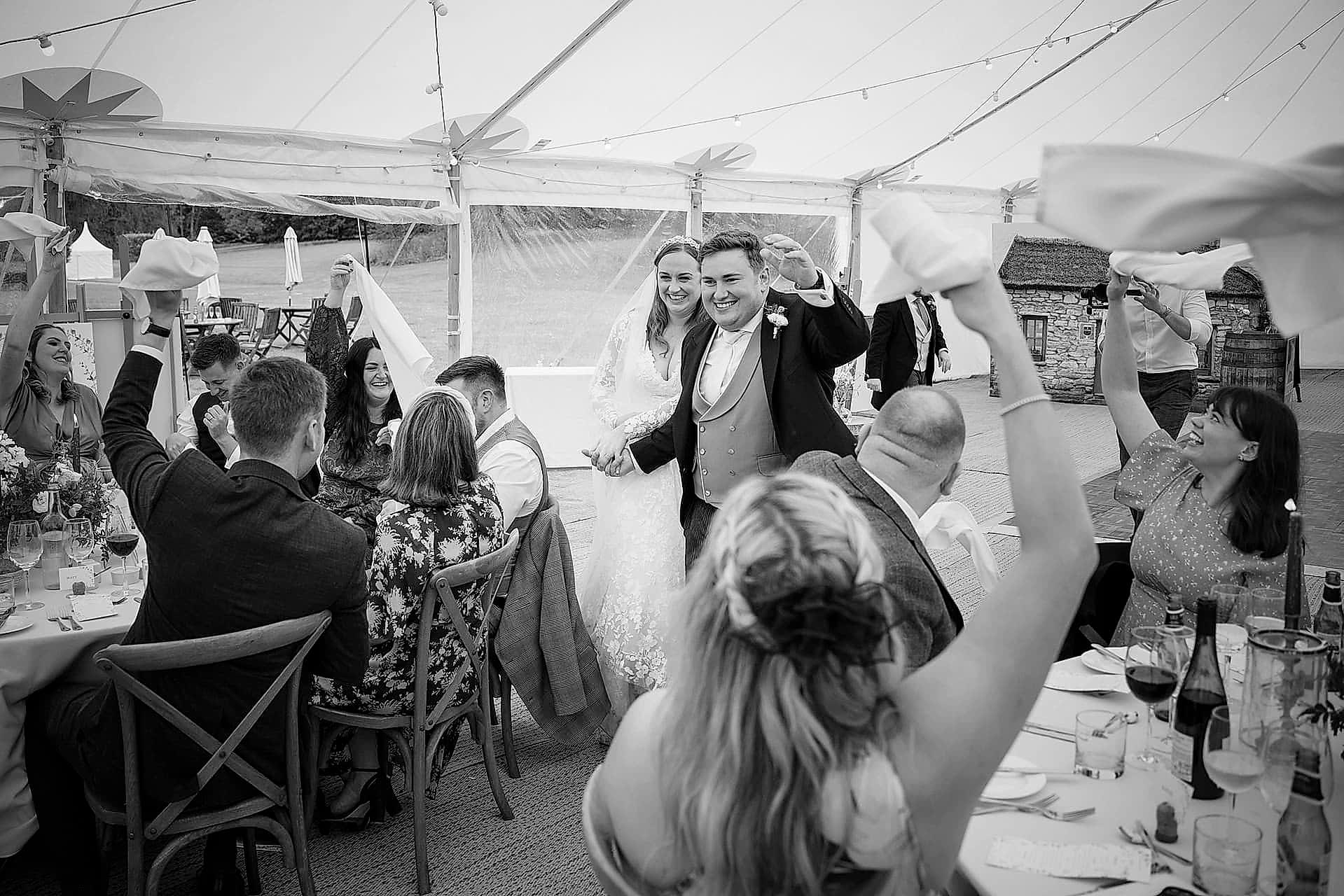 Wedding guests waving their napkins as the bride and groom make their entrance for the wedding breakfast