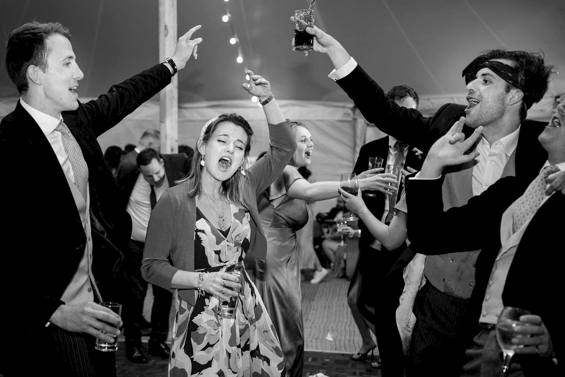 Wedding guests dancing with their hands and drinks in the air