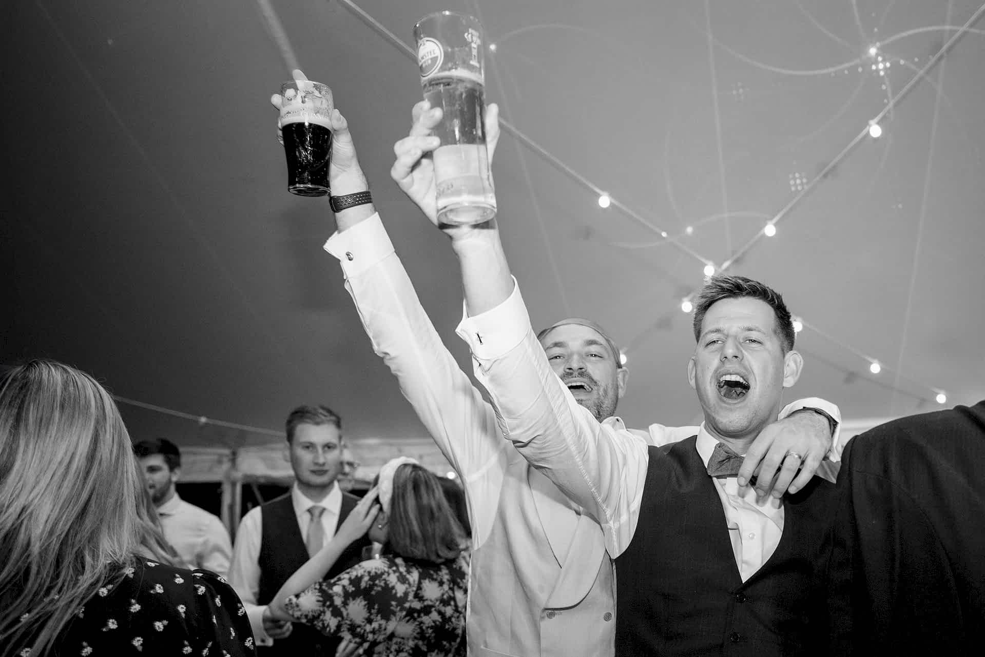 Two wedding guests singing and holding their drinks in the air as they dance