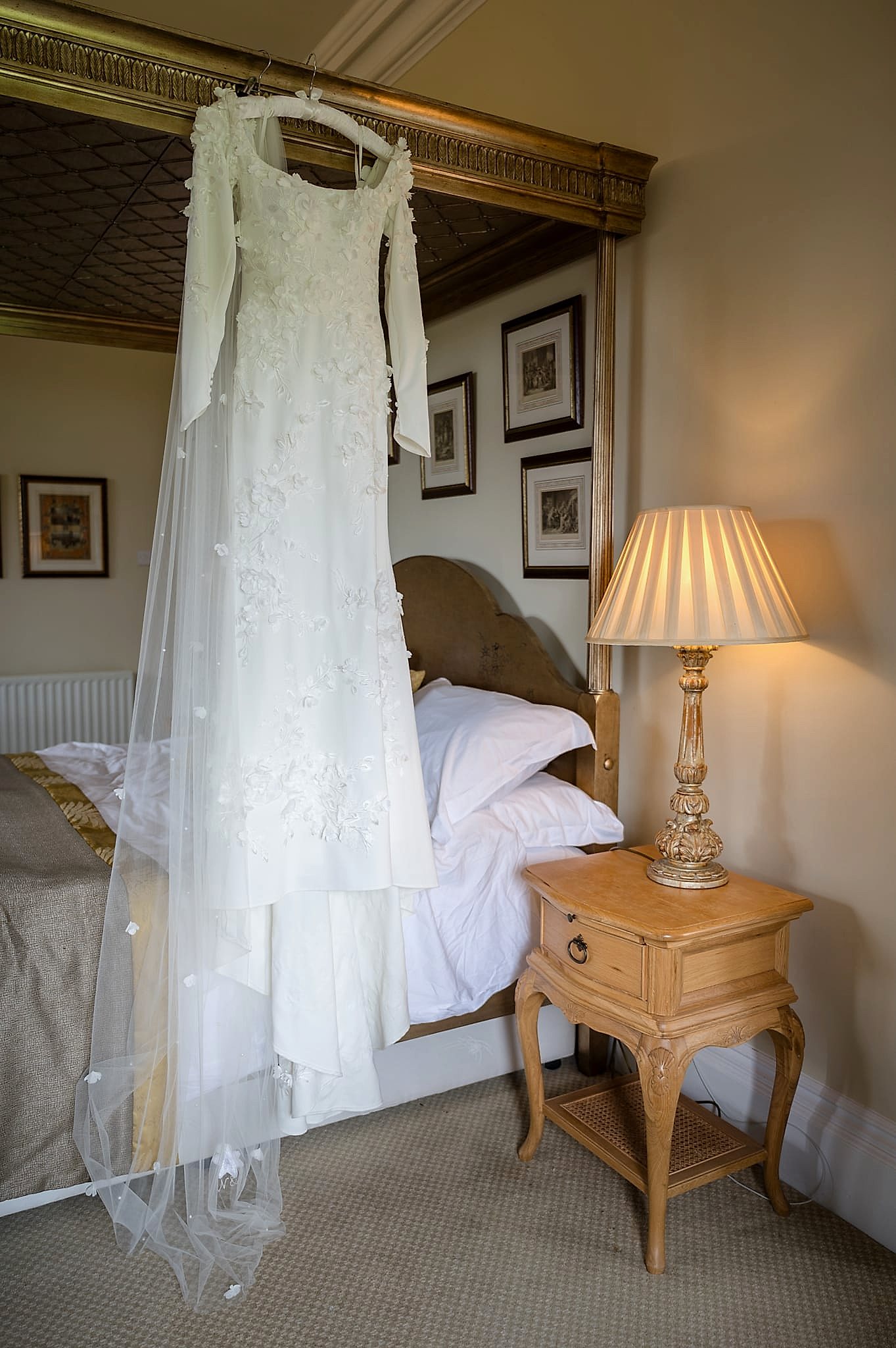 A Kelly Faetanini wedding dress hanging on the rail of a four posted bed at Fawsley Hall