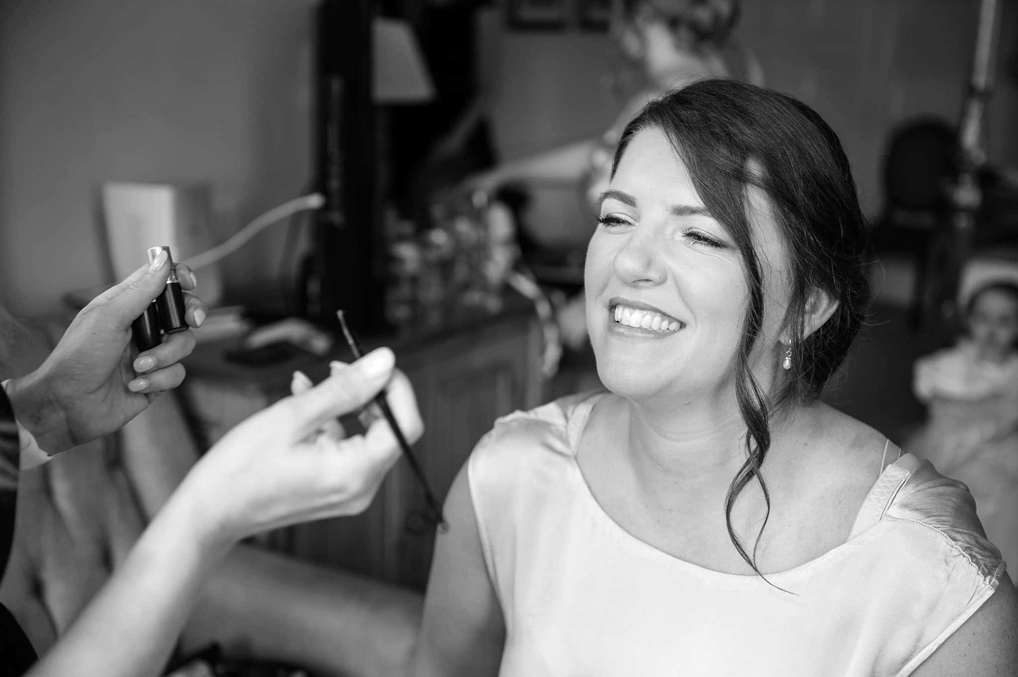 A bridesmaid smiling as a makeup artist applies her lipstick