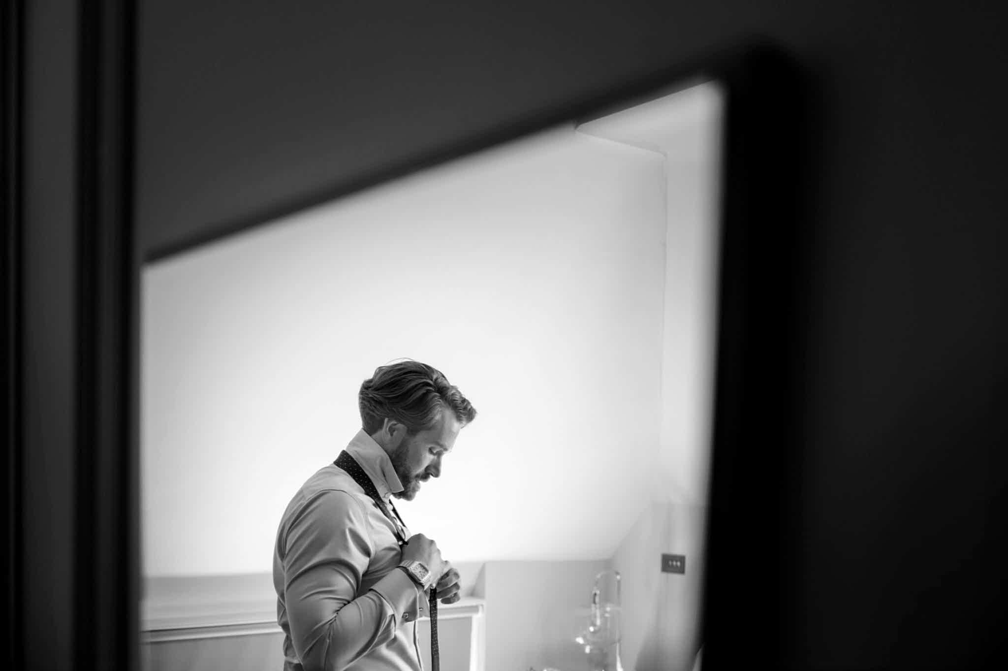 A mirror reflection of a groom putting on his tie