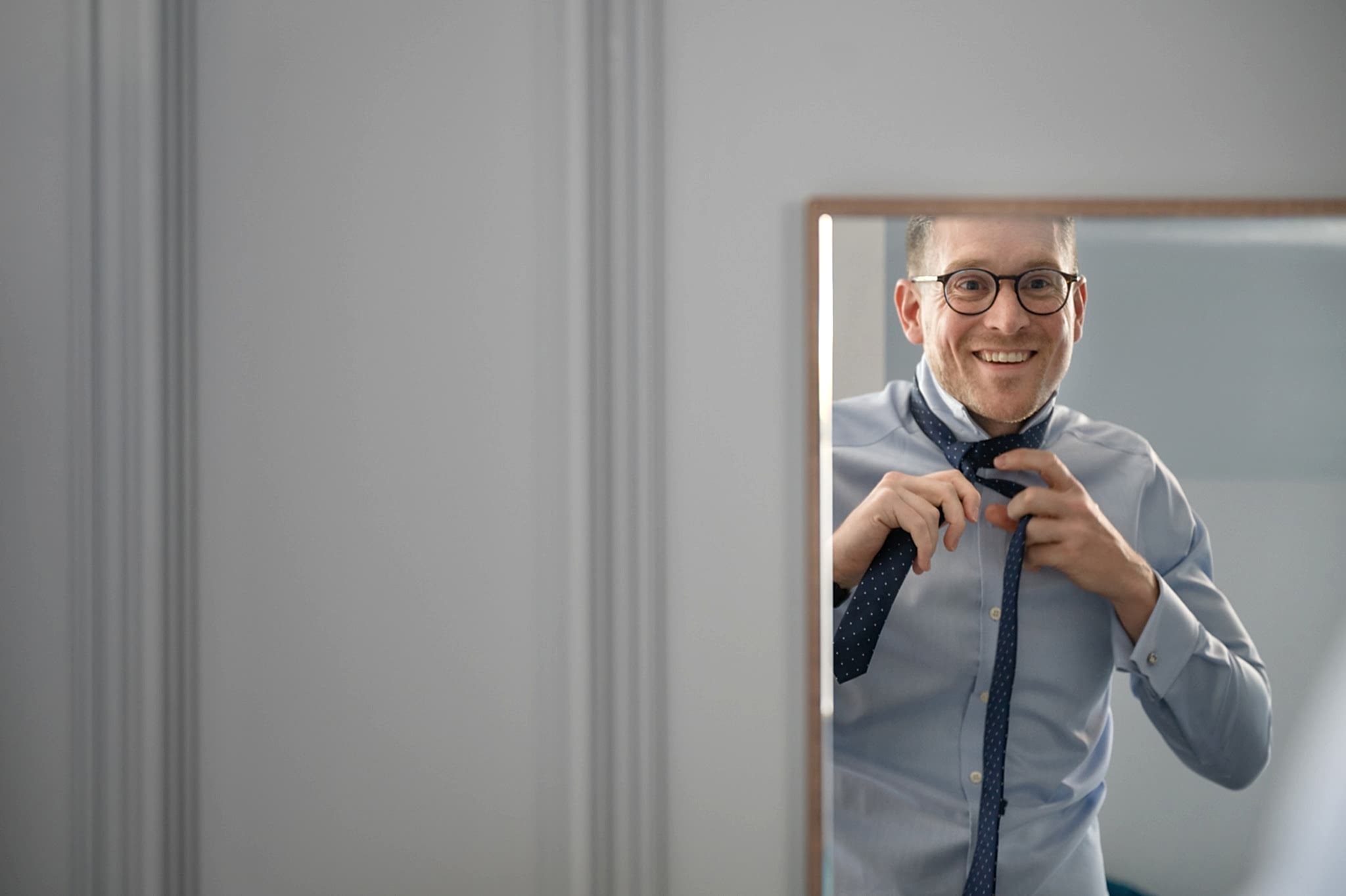 A mirror reflection of an usher smiling as he puts on his tie