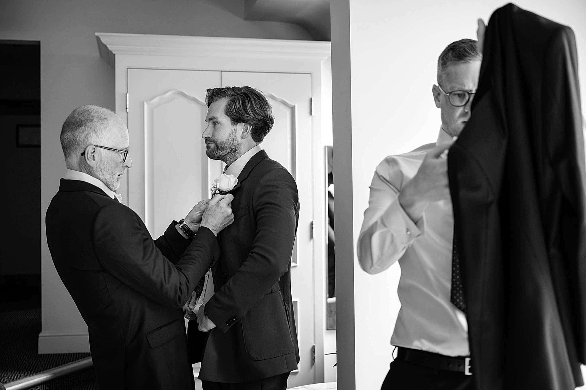 The groom's dad pinning on the groom's buttonhole while his brother tries to do his own