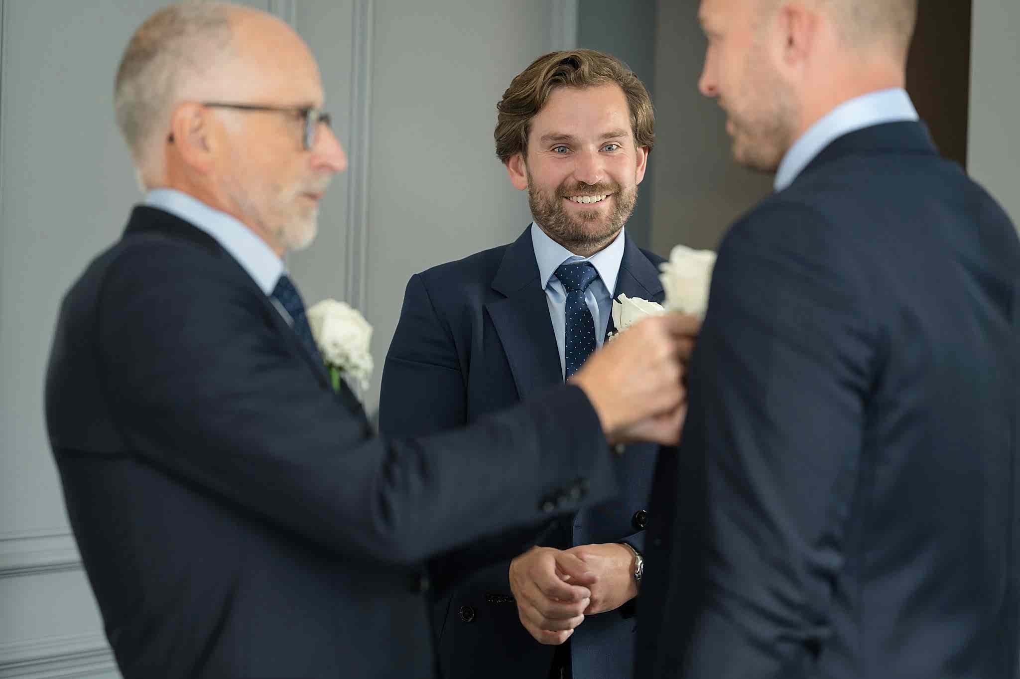 The groom looking on with a smile as his dad pins on his brother's buttonhole
