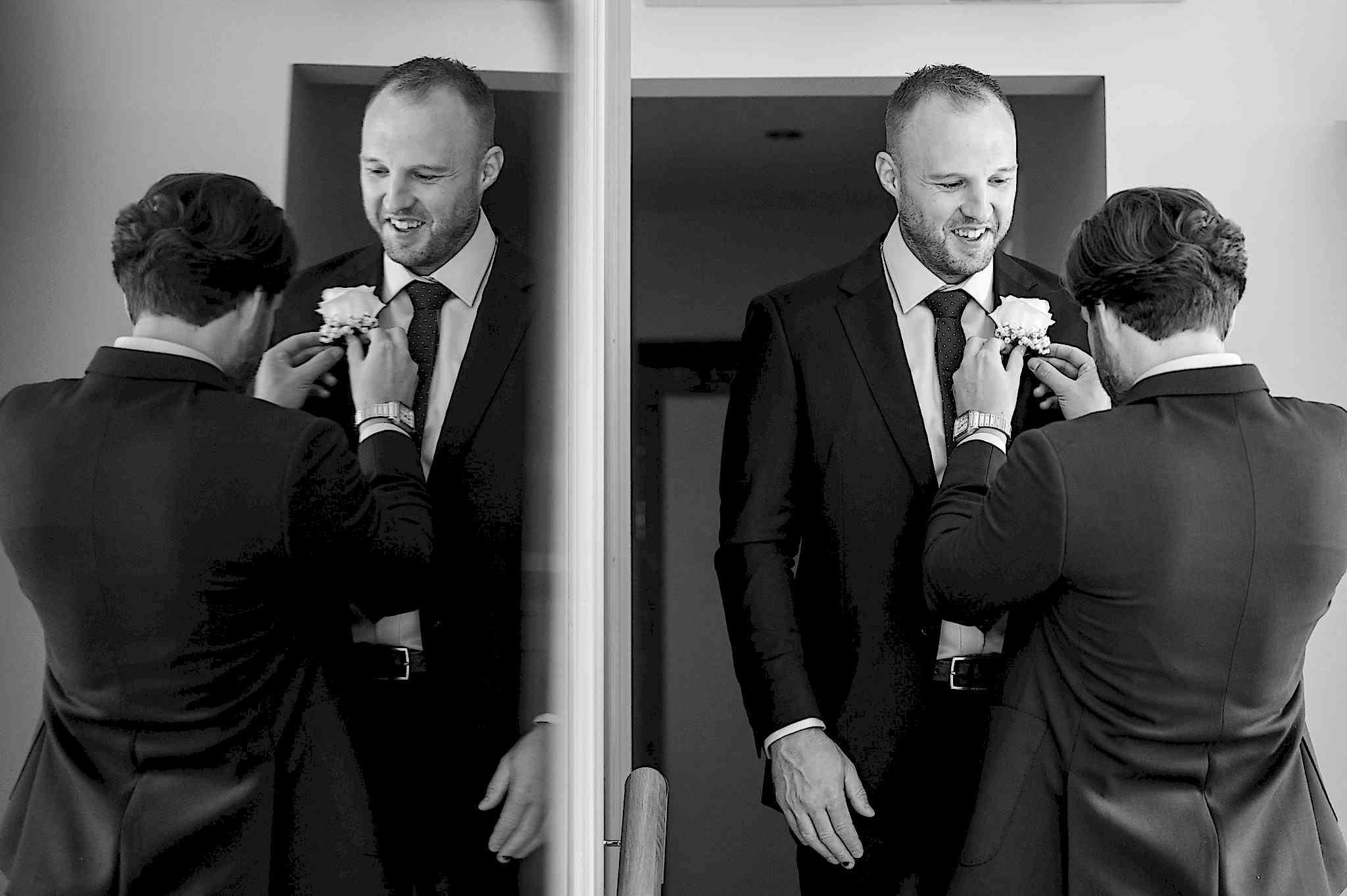 The groom putting on the best man's buttonhole with the image reflected in a mirror