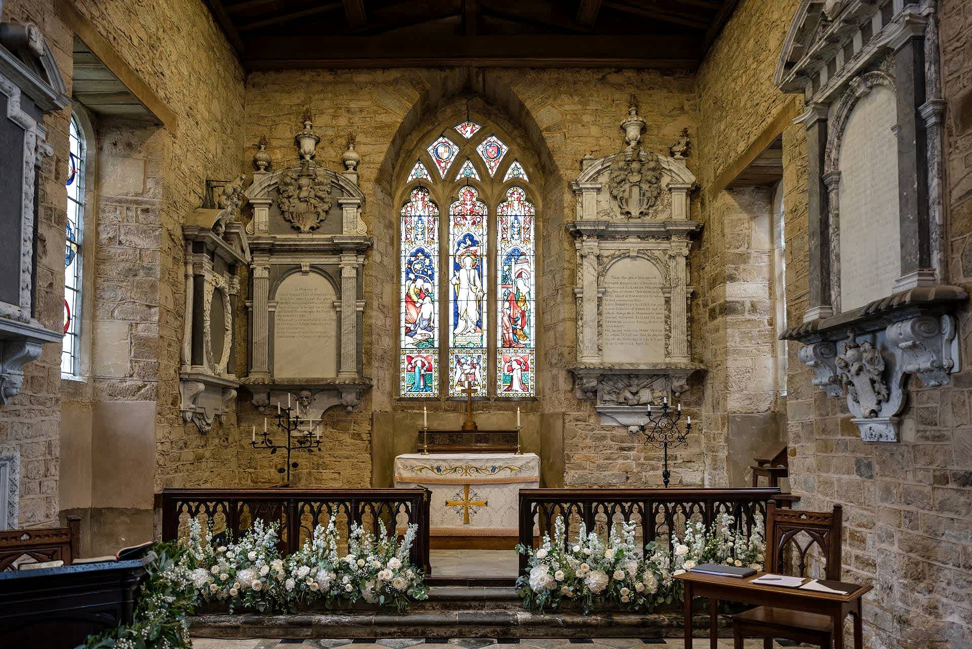 The altar at Fawsley church decorated with fresh white flowers and green foliage ready for a wedding