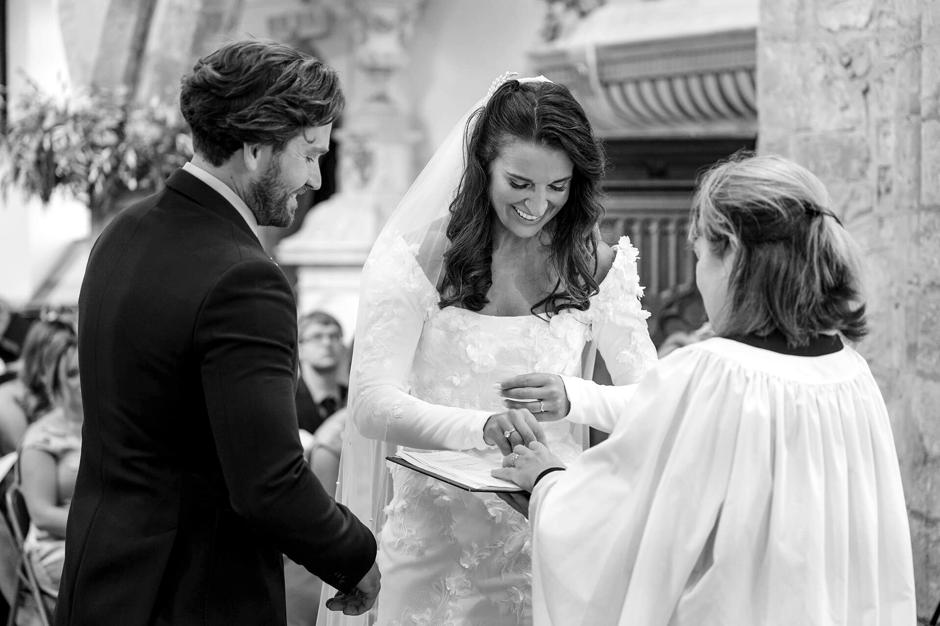 The bride taking the groom's ring from the vicar at Fawsley church