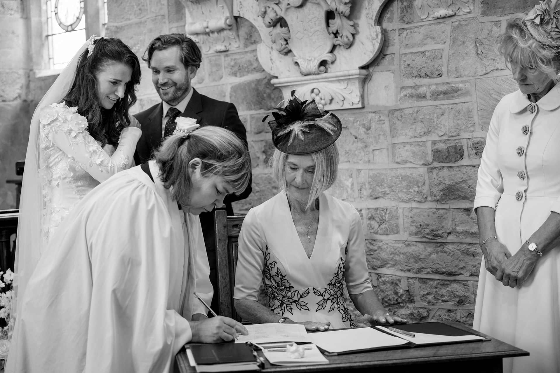 The bride and groom looking on as their mum's sign the marriage register at Fawsley church