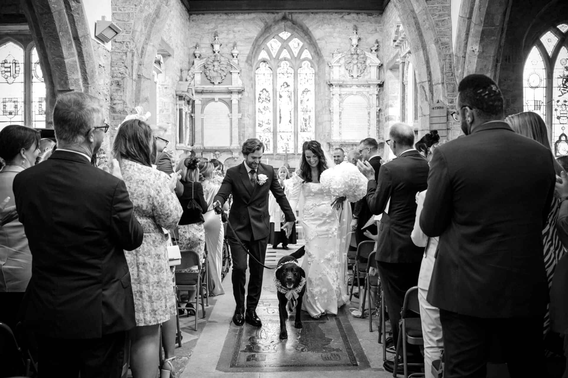 The bride and groom walking down the aisle with their dog at Fawsley church