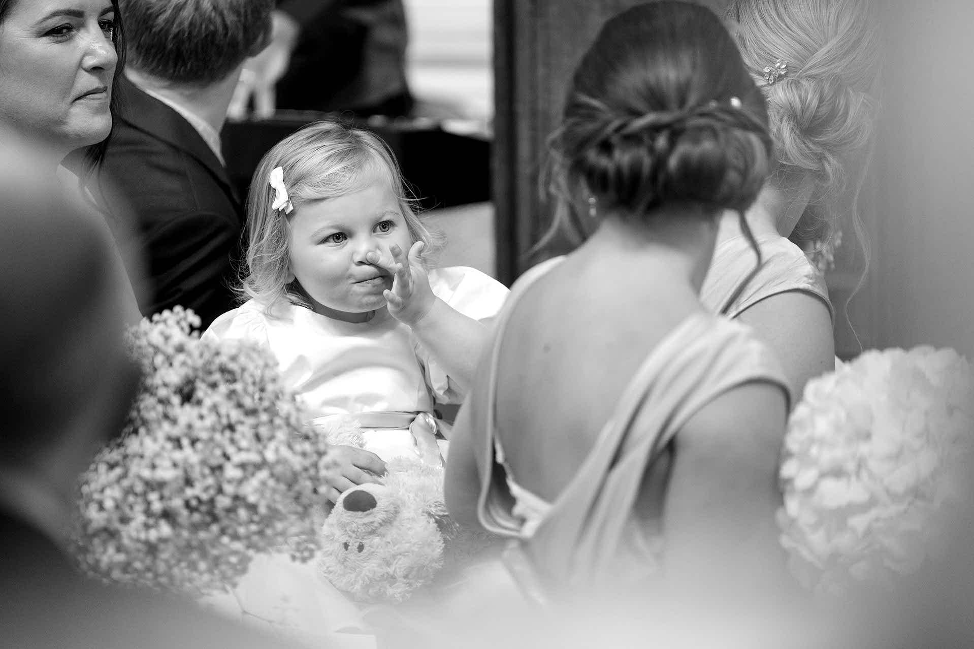 A little flower girl touching her nose as she plays 'Simon Says' with a bridesmaid