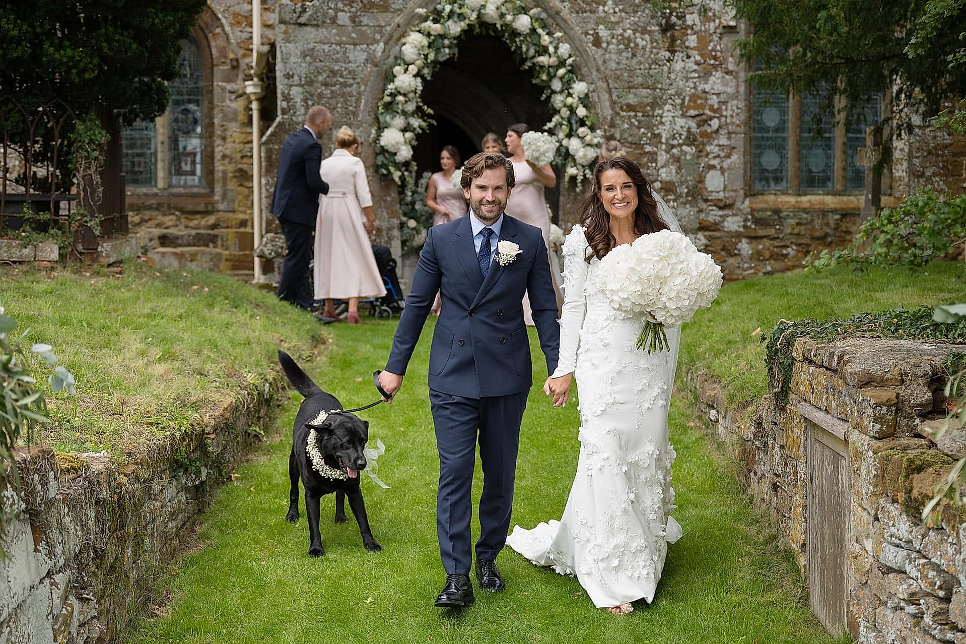 Bride and groom walking out of Fawsley church with their dog