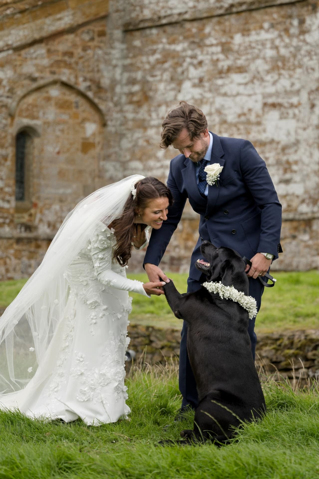 Bride and groom enjoying a moment to play with their dog outside Fawsley church