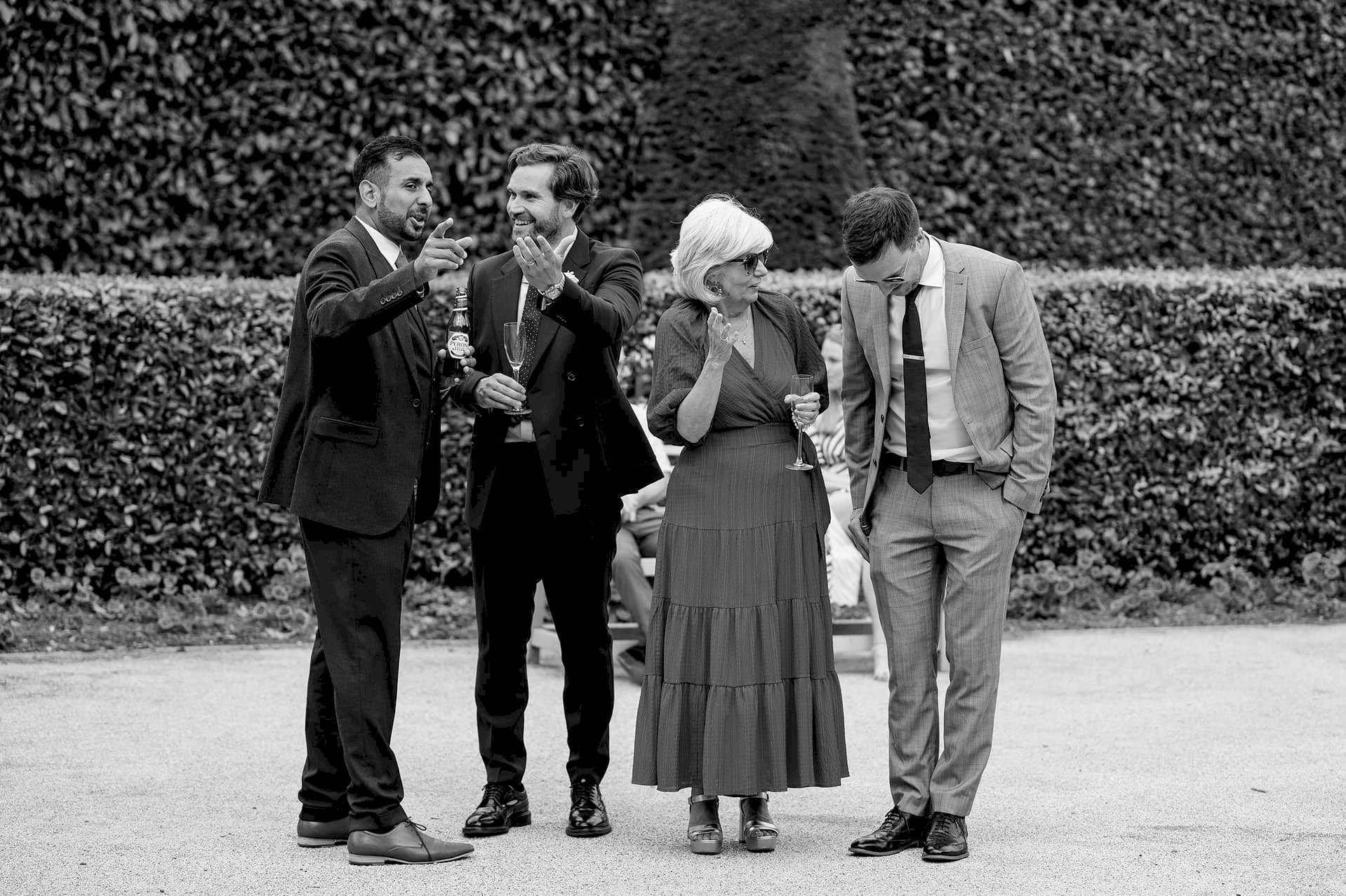 Wedding guests chatting to the groom during the drinks reception outside Knightley Court at Fawsley Hall