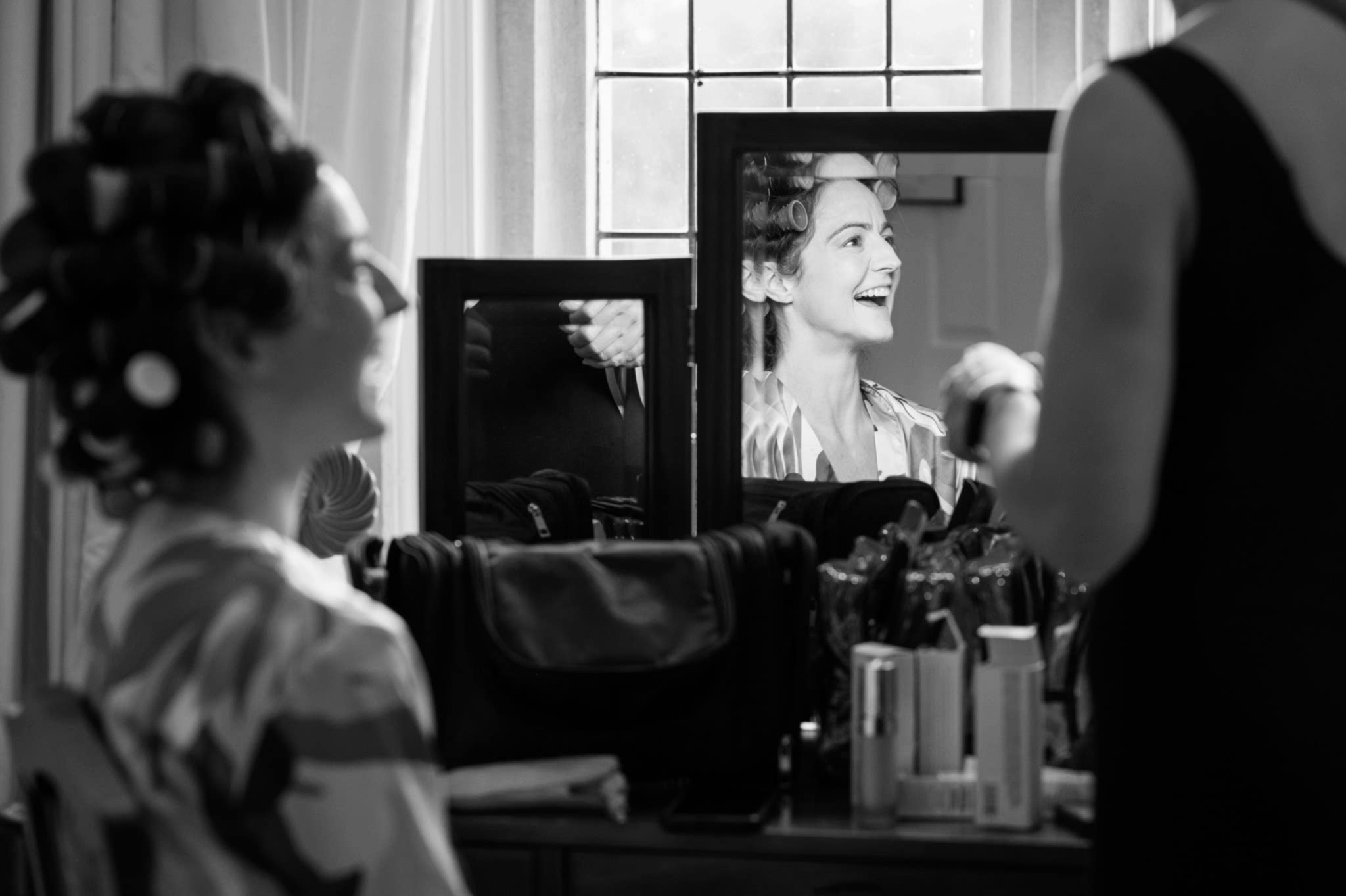 A mirror reflection of the bride laughing as she has her makeup done