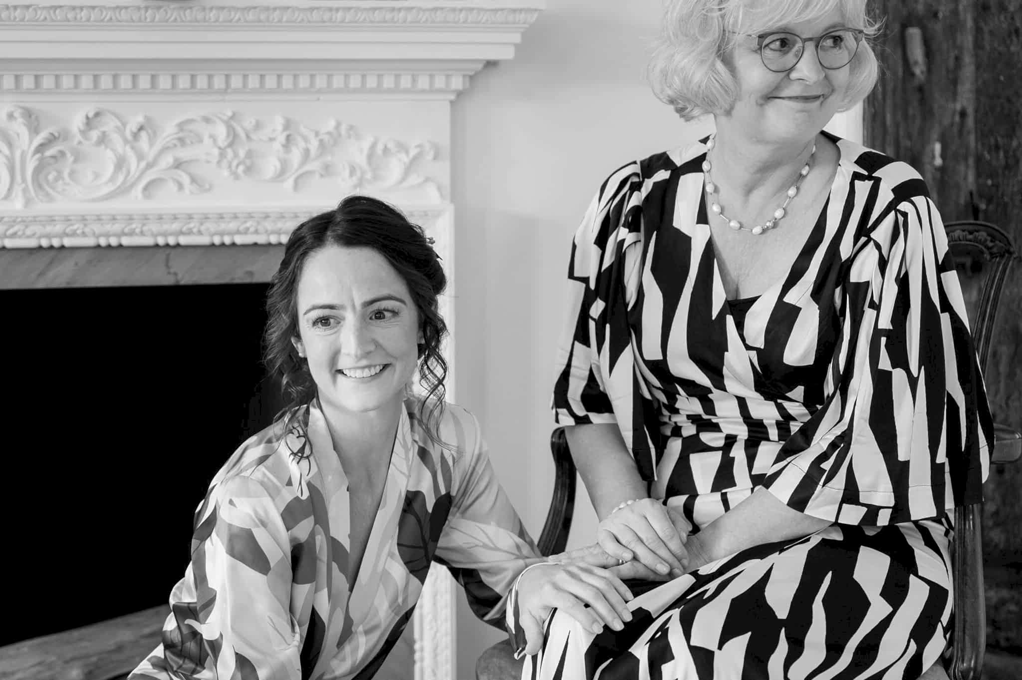 Bride crouching next to her mum who is sitting on a chair and the two are holding hands in a quiet moment together