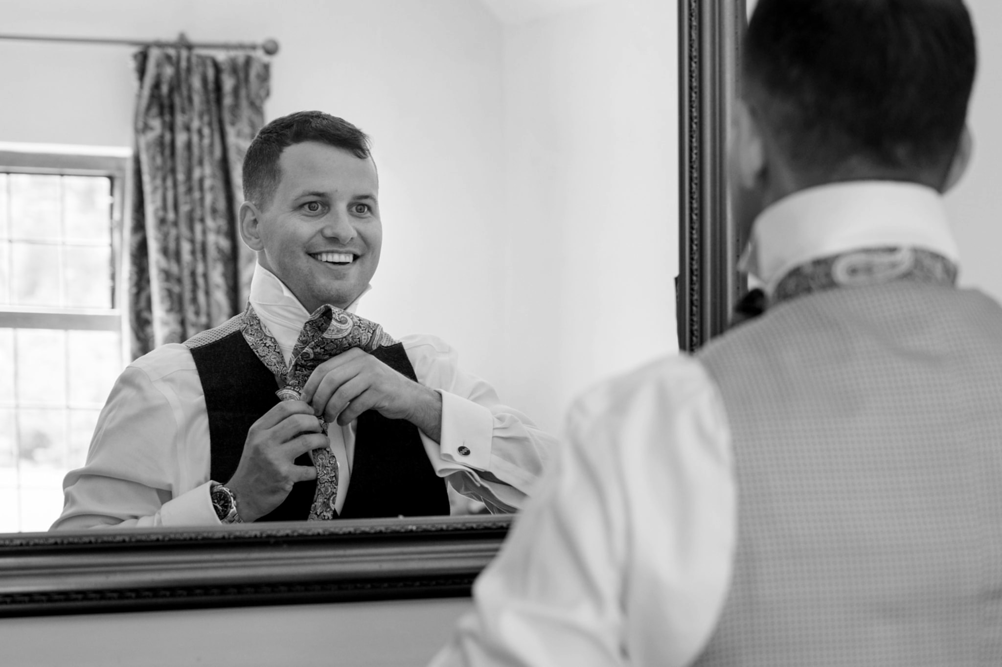 The groom looking in a mirror to put on his tie