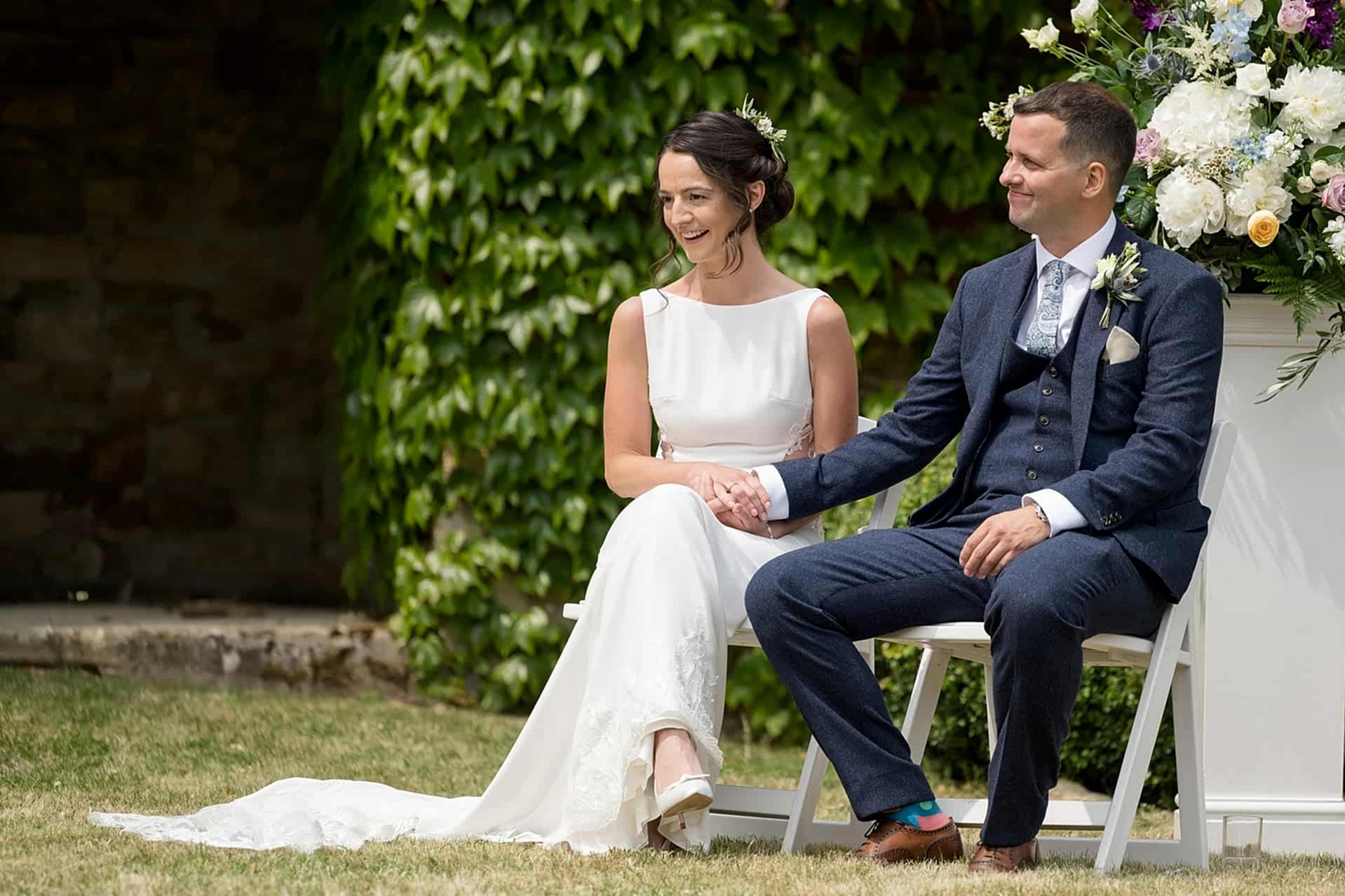 The bride and groom sitting together and holding hands as the celebrant talks during their wedding ceremony