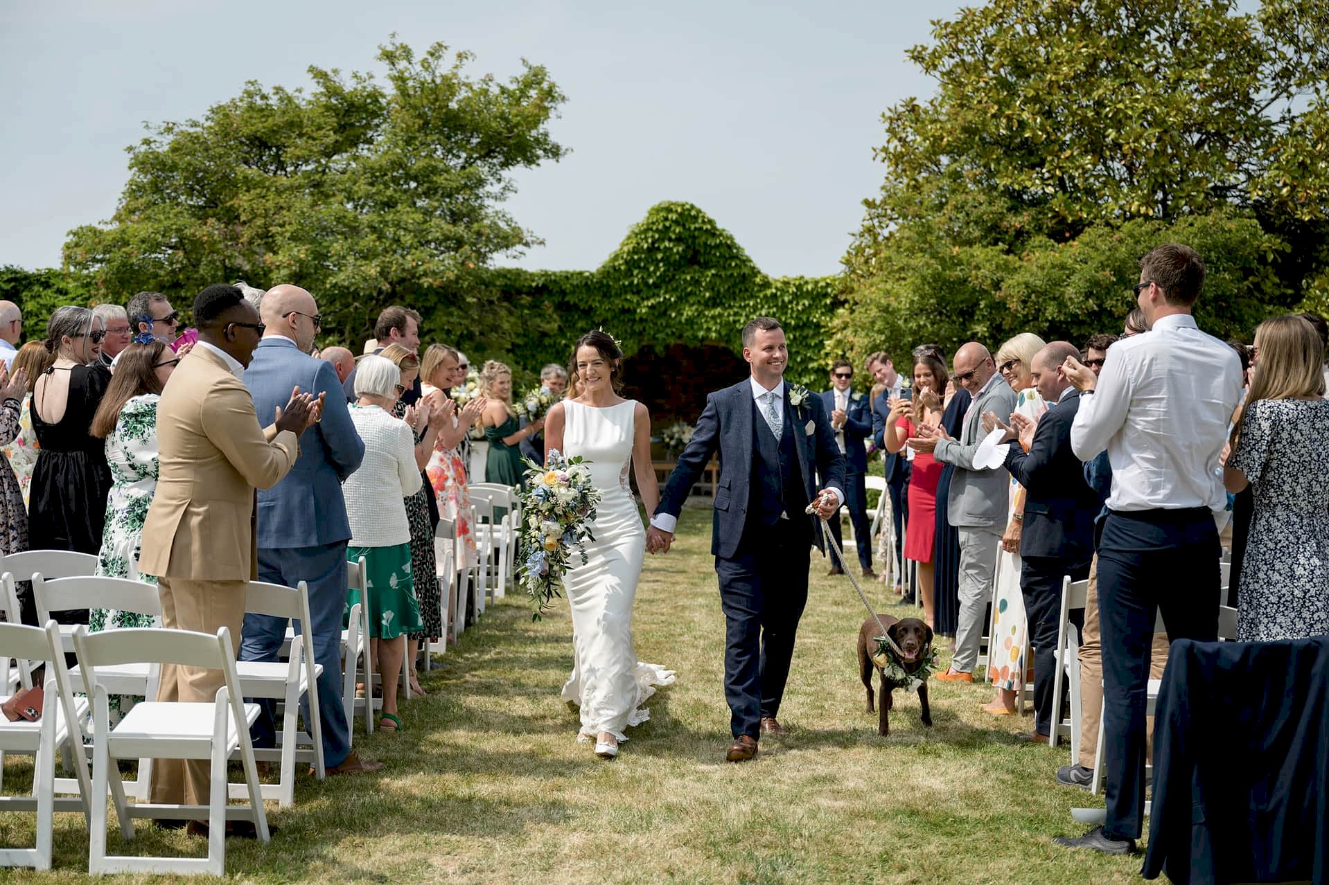 Bride and groom walking down the aisle with their dog after an outdoor ceremony at Notley Abbey