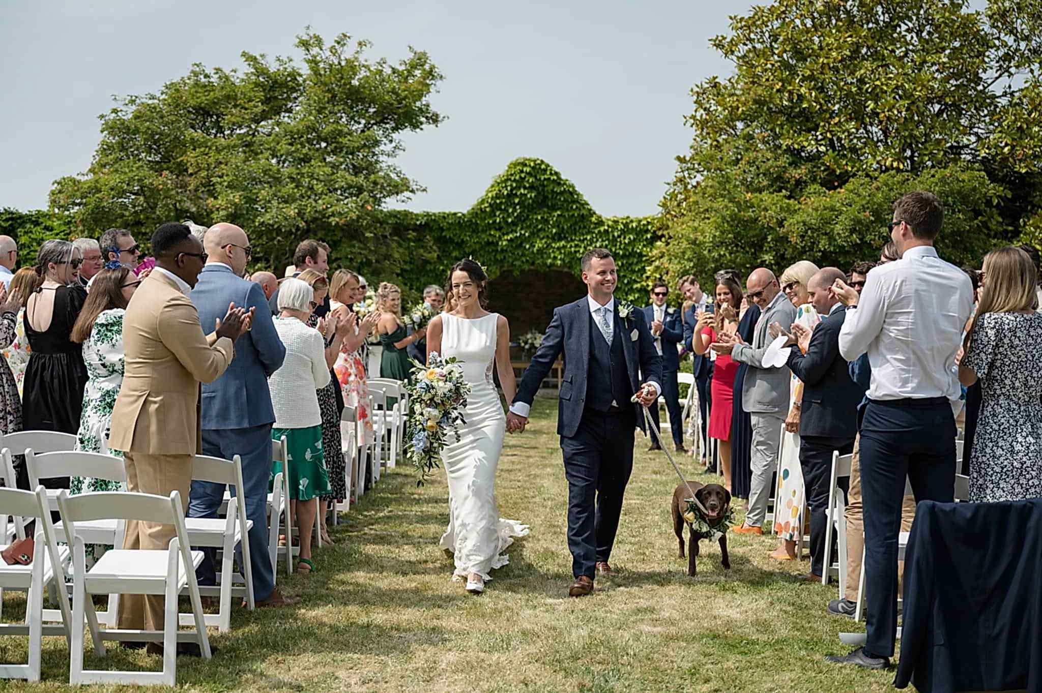 Bride and groom walking down the aisle with their dog after an outdoor ceremony at Notley Abbey