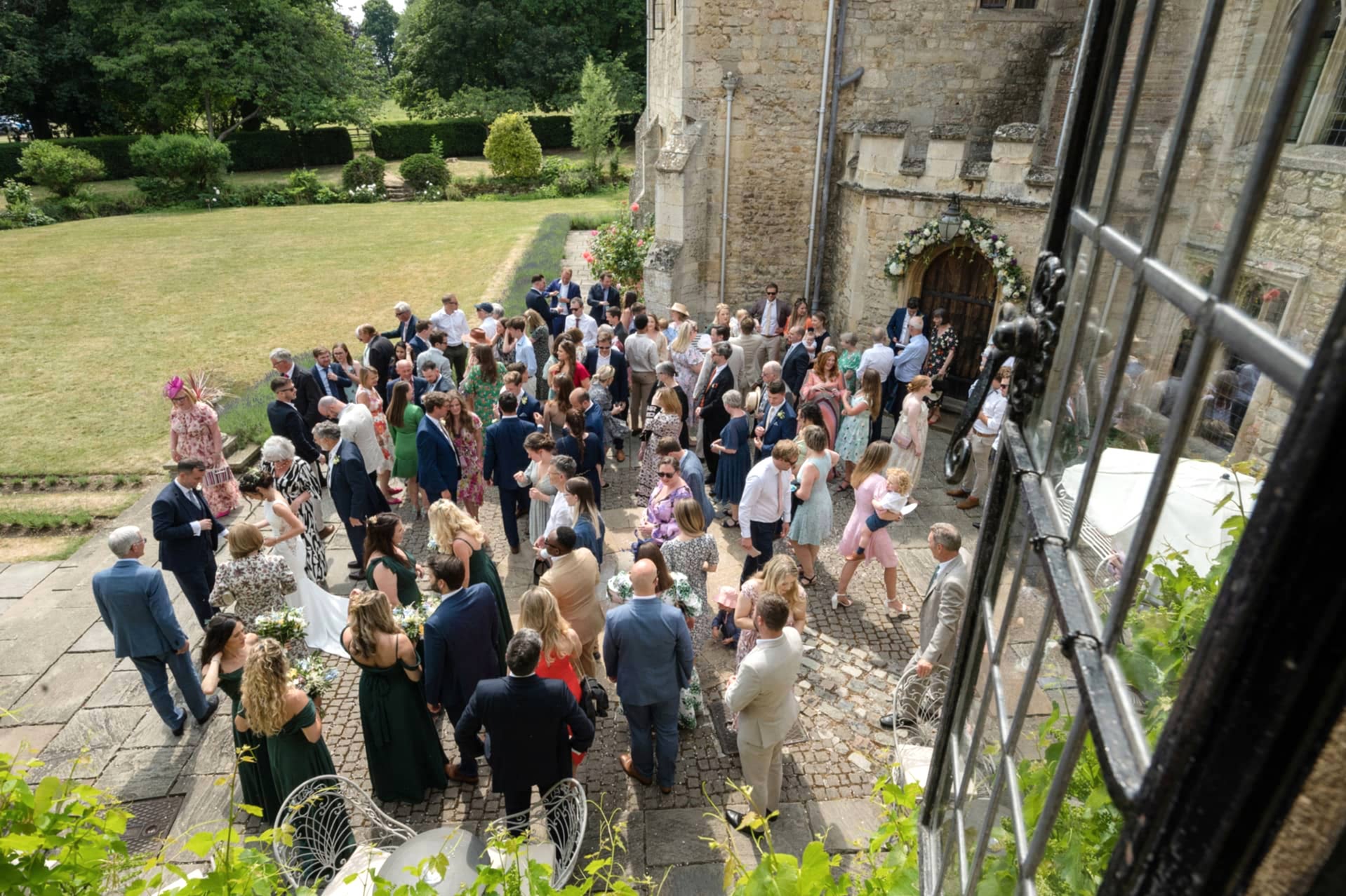 A wide-angle view of a wedding drinks reception taken from an upstairs window at Notley Abbey