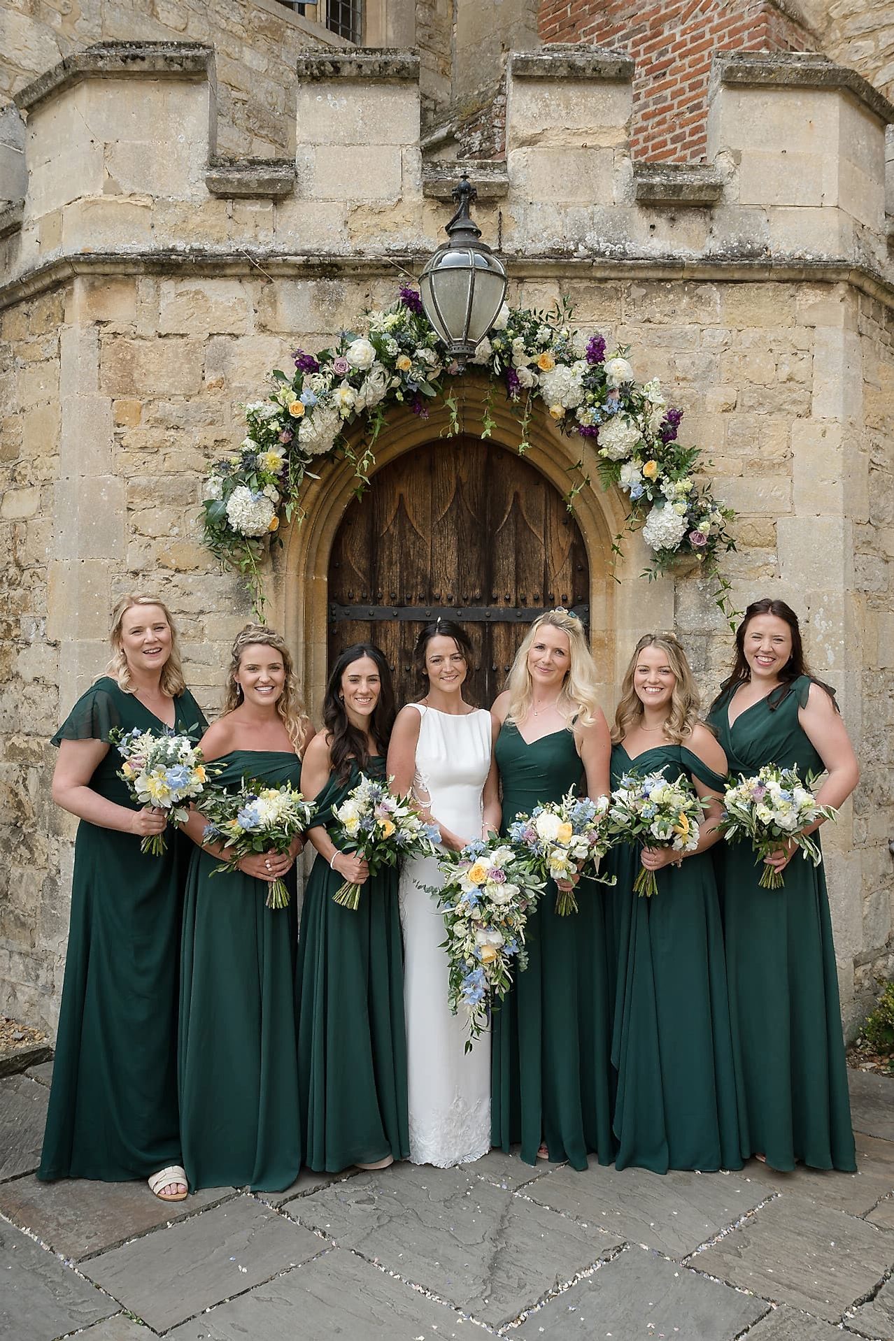 The bride and her bridesmaids posing for a group photo outside the front door of Notley Abbey