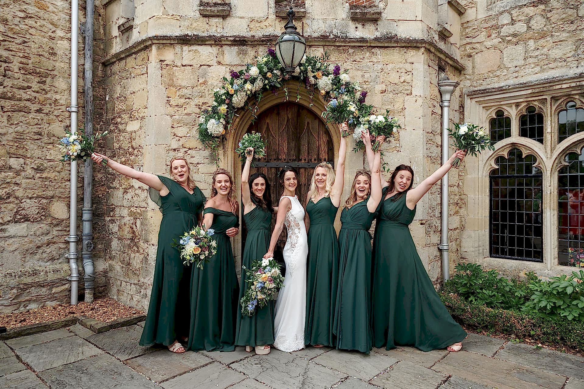 The bride and her bridesmaids posing for a group photo outside the front door of Notley Abbey