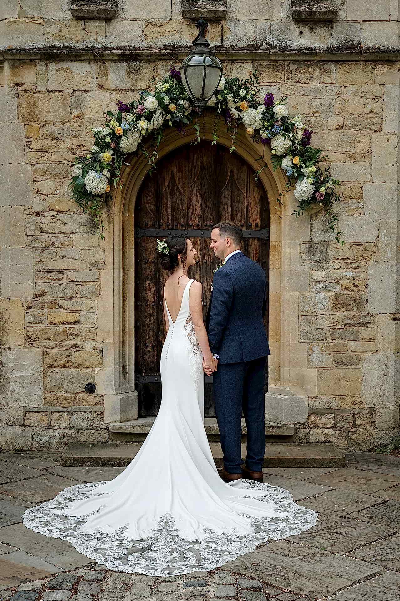 A posed photo of the bride and groom showing the bride's train at the front door of Notley Abbey
