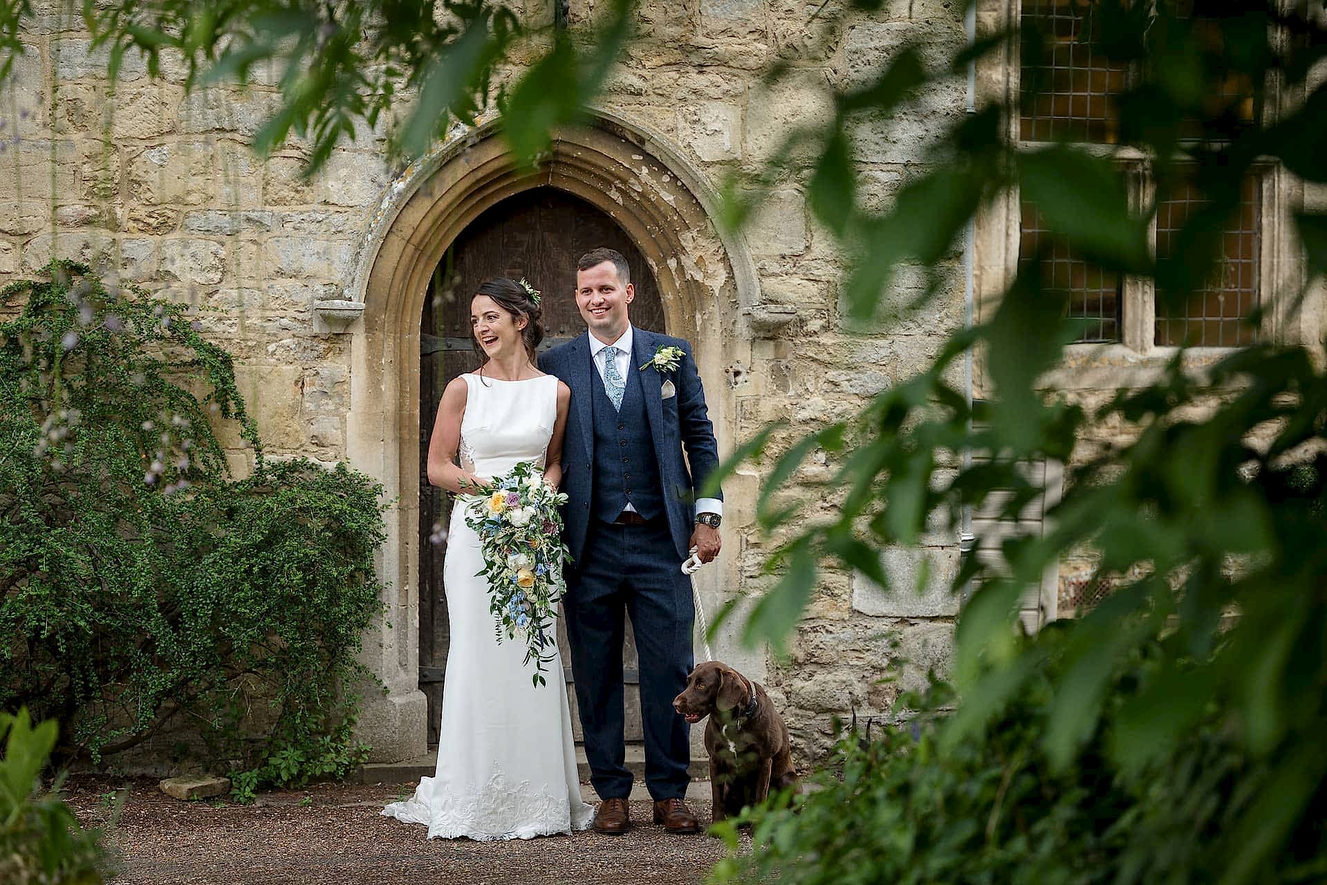 The bride and groom standing with their dog at the back door of Notley Abbey
