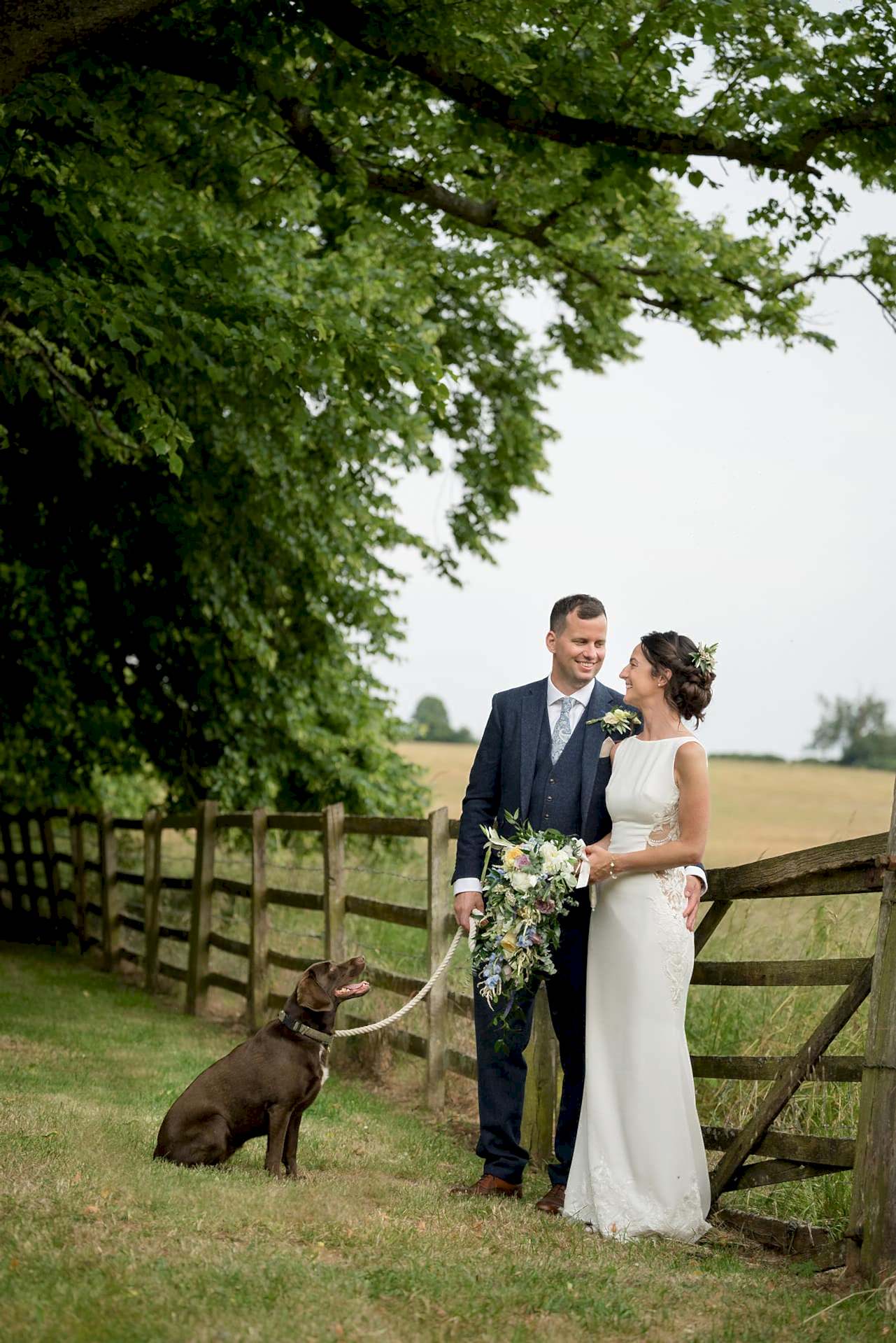 Bride and groom chatting by a fence with their dog at Notley Abbey