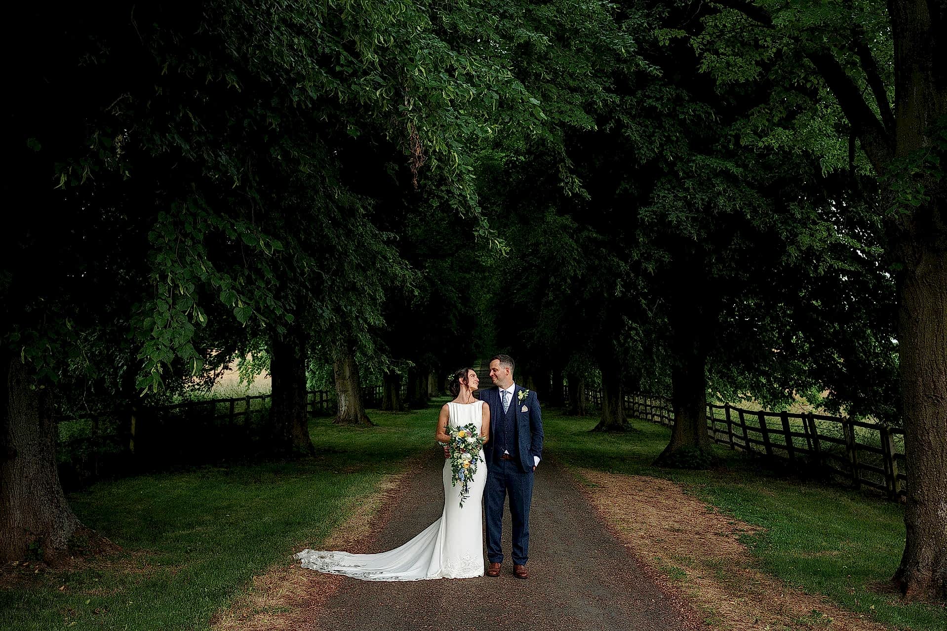 The bride and groom posing for a photo on the tree-lined avenue at Notley Abbey