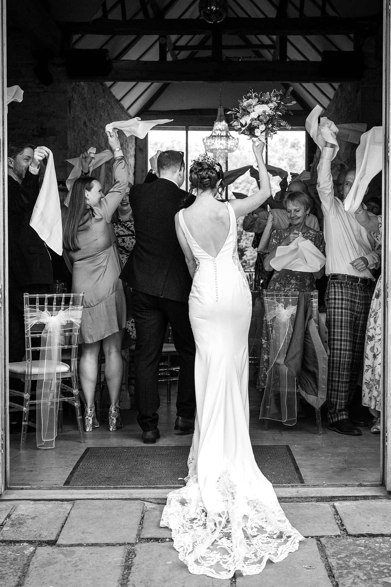Guests waving their napkins as the bride and groom walking into the Monk's Refectory at Notley Abbey for their wedding breakfast